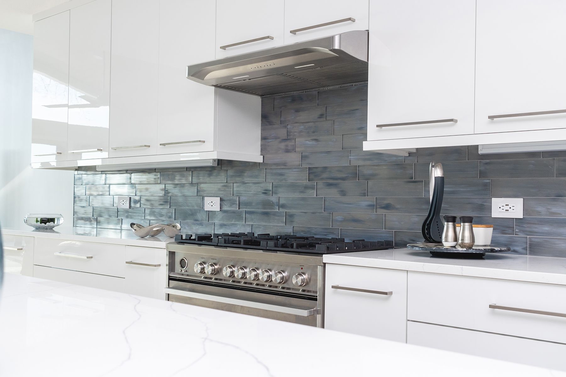Modern white kitchen with stainless steel stove, hood, and blue glass backsplash