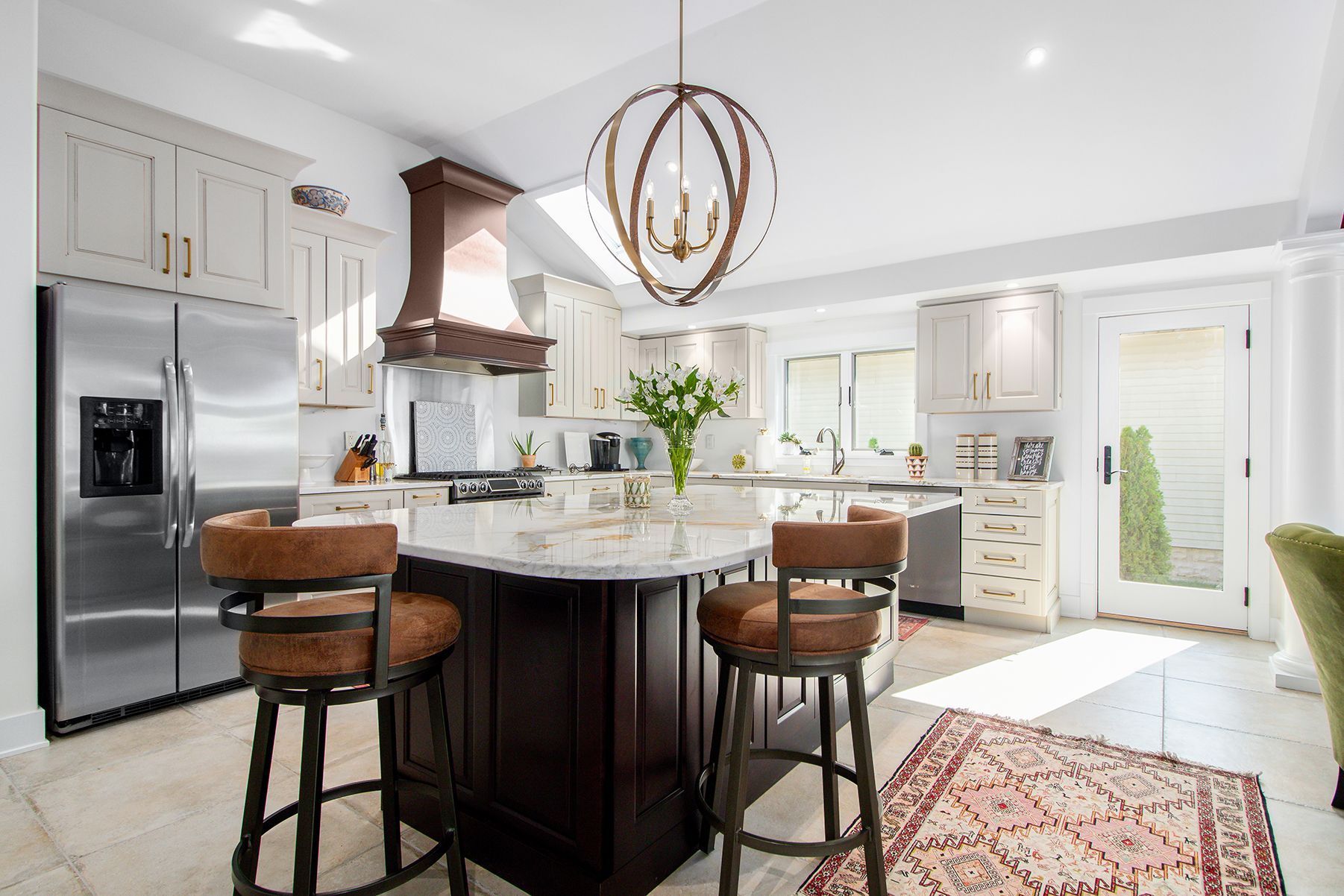 A kitchen with a large island , stools , a refrigerator , and a rug.