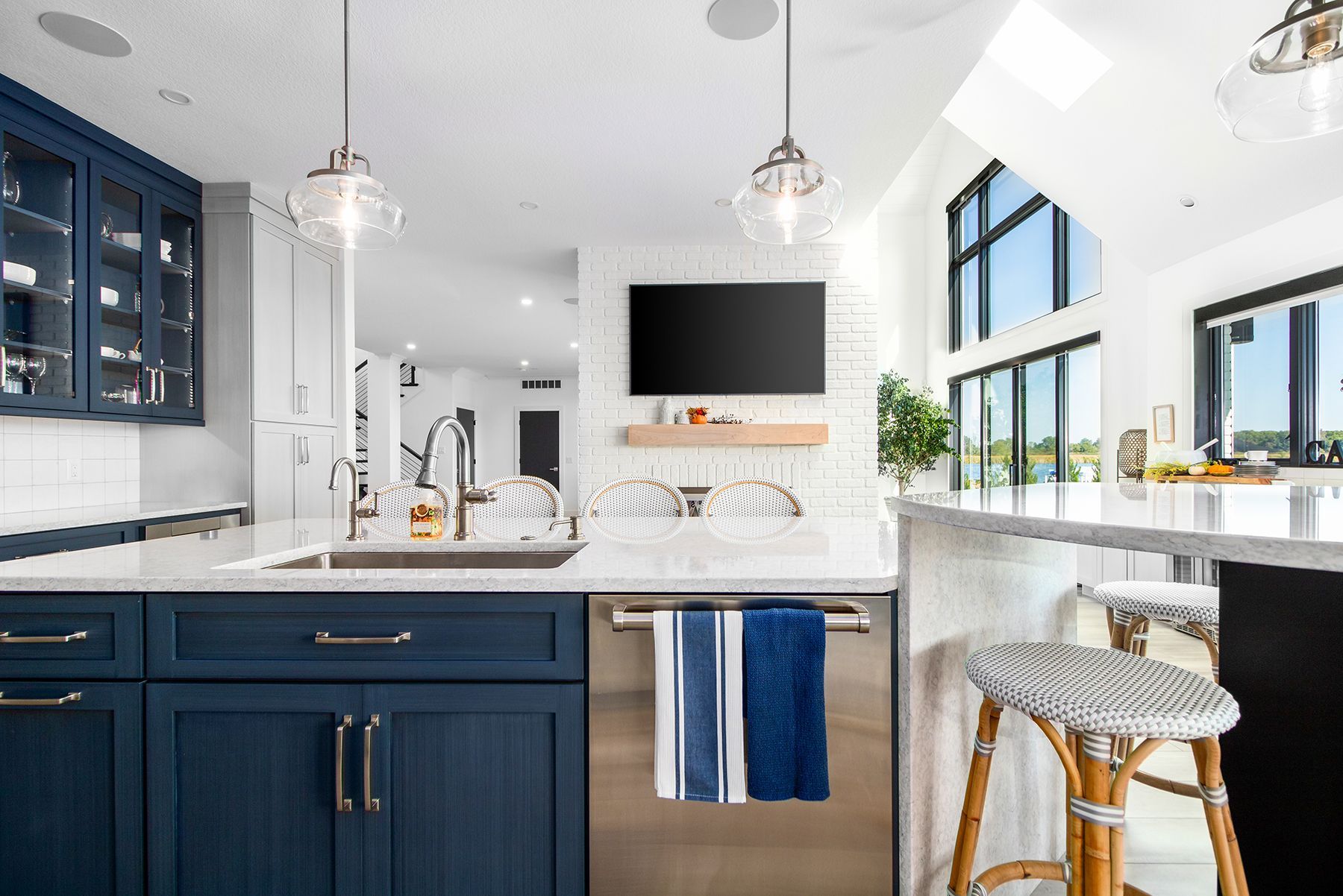 Bright modern kitchen with navy cabinets, white island, pendant lights, and a stool by large windows