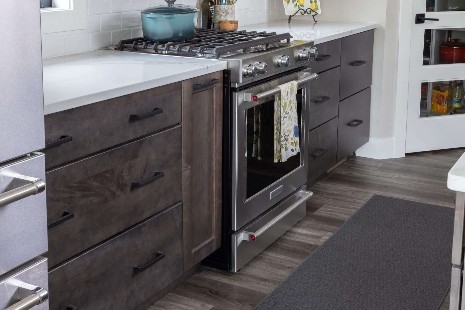 Modern kitchen with dark cabinets, white countertop, gas stove, and gray floor runner