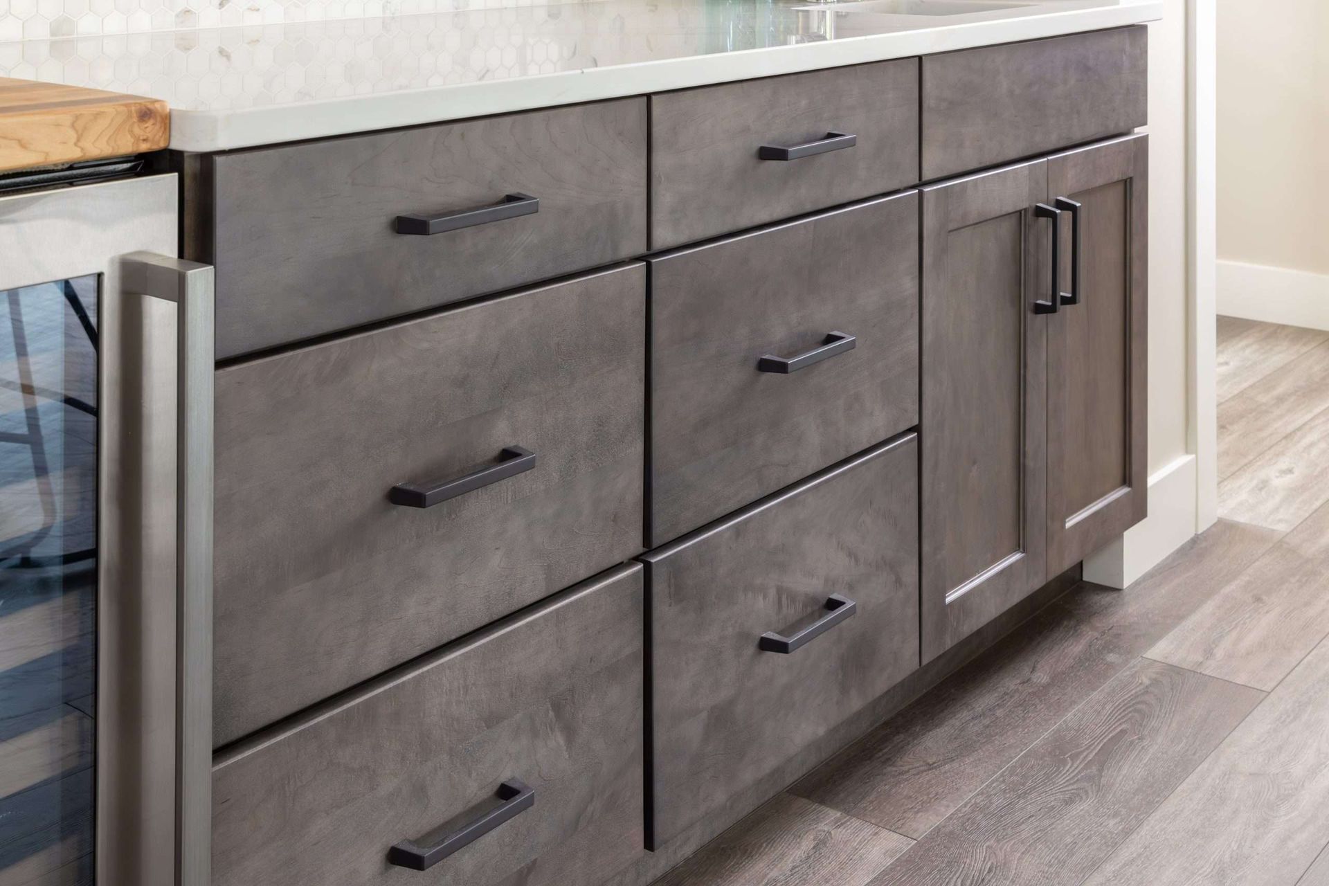 Gray kitchen cabinets with black handles under a countertop, viewed from the side.