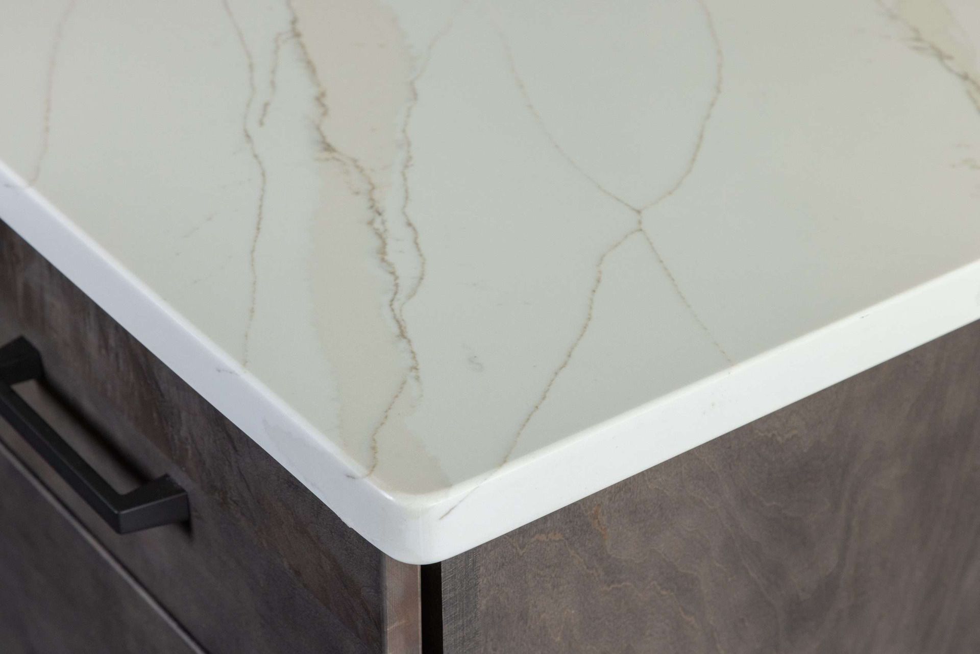 Close-up of a white marble-look countertop edge on dark wood cabinetry with a black handle