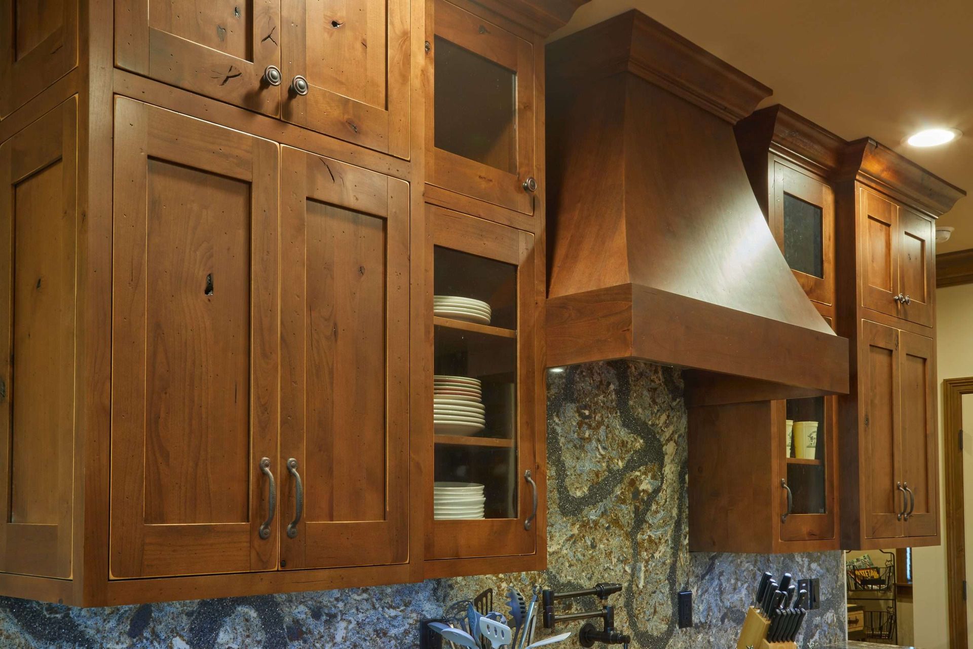 Wooden kitchen cabinets with a central range hood and stone backsplash.
