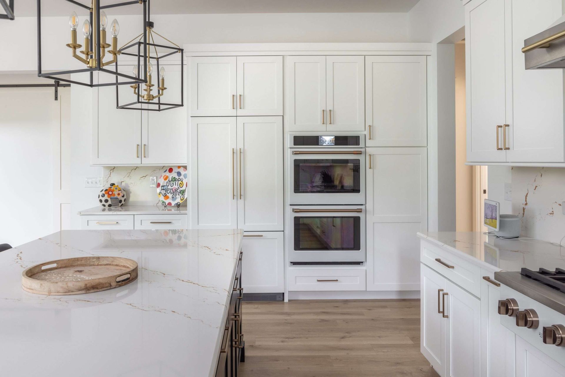 Bright white modern kitchen with island, built-in ovens, and gold light fixture