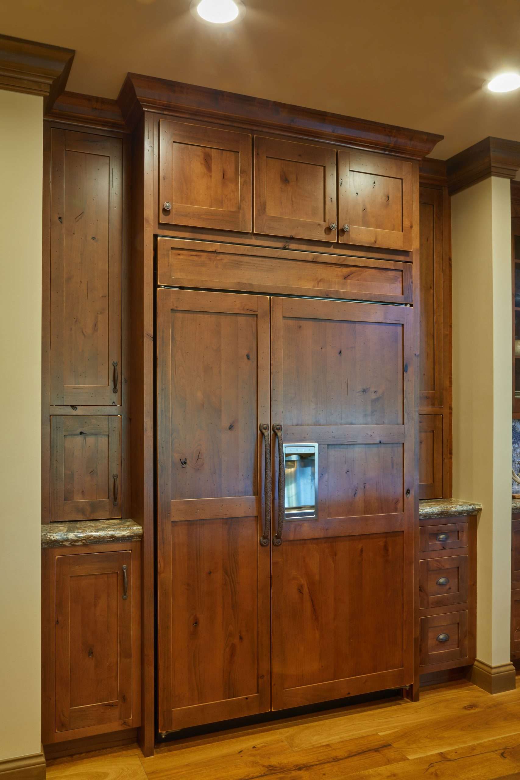 Large wooden built-in cabinet with central refrigerator, set in a warm-toned kitchen nook.