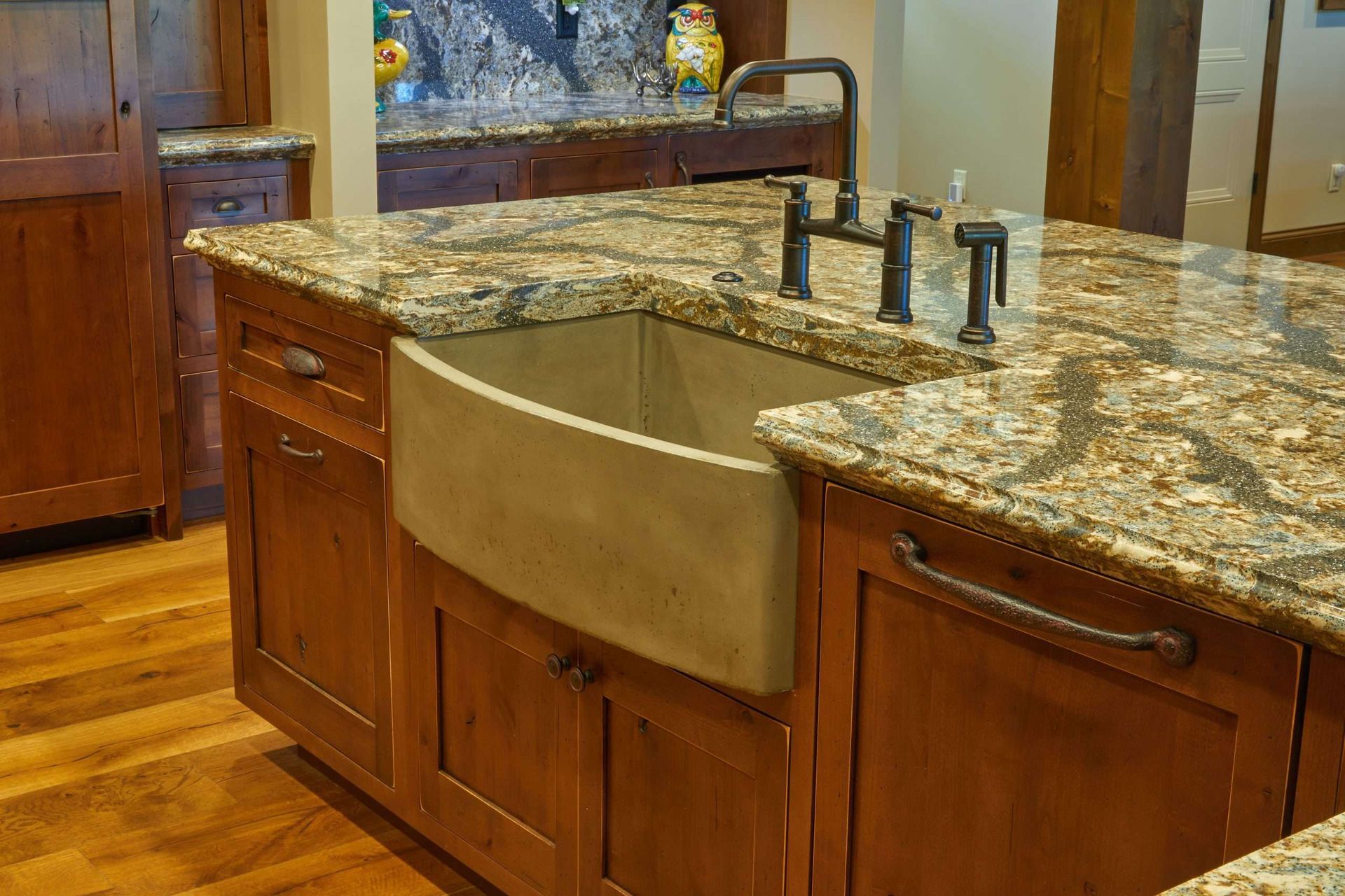 Kitchen island with a large farmhouse sink, wood cabinets, and granite countertop in a warm-toned kitchen