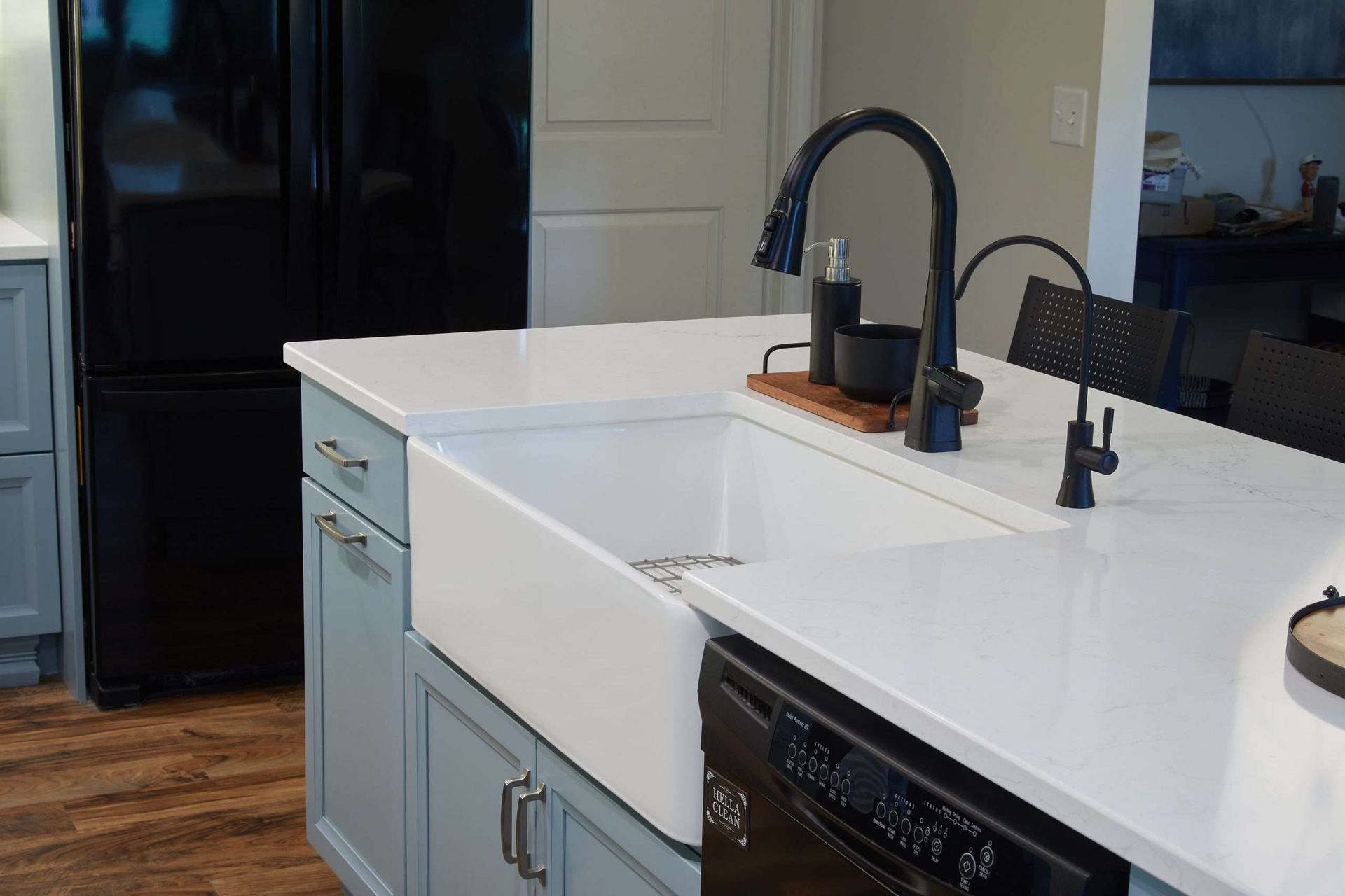 Modern kitchen island with white countertop, black faucet, and blue cabinetry near a dark refrigerator