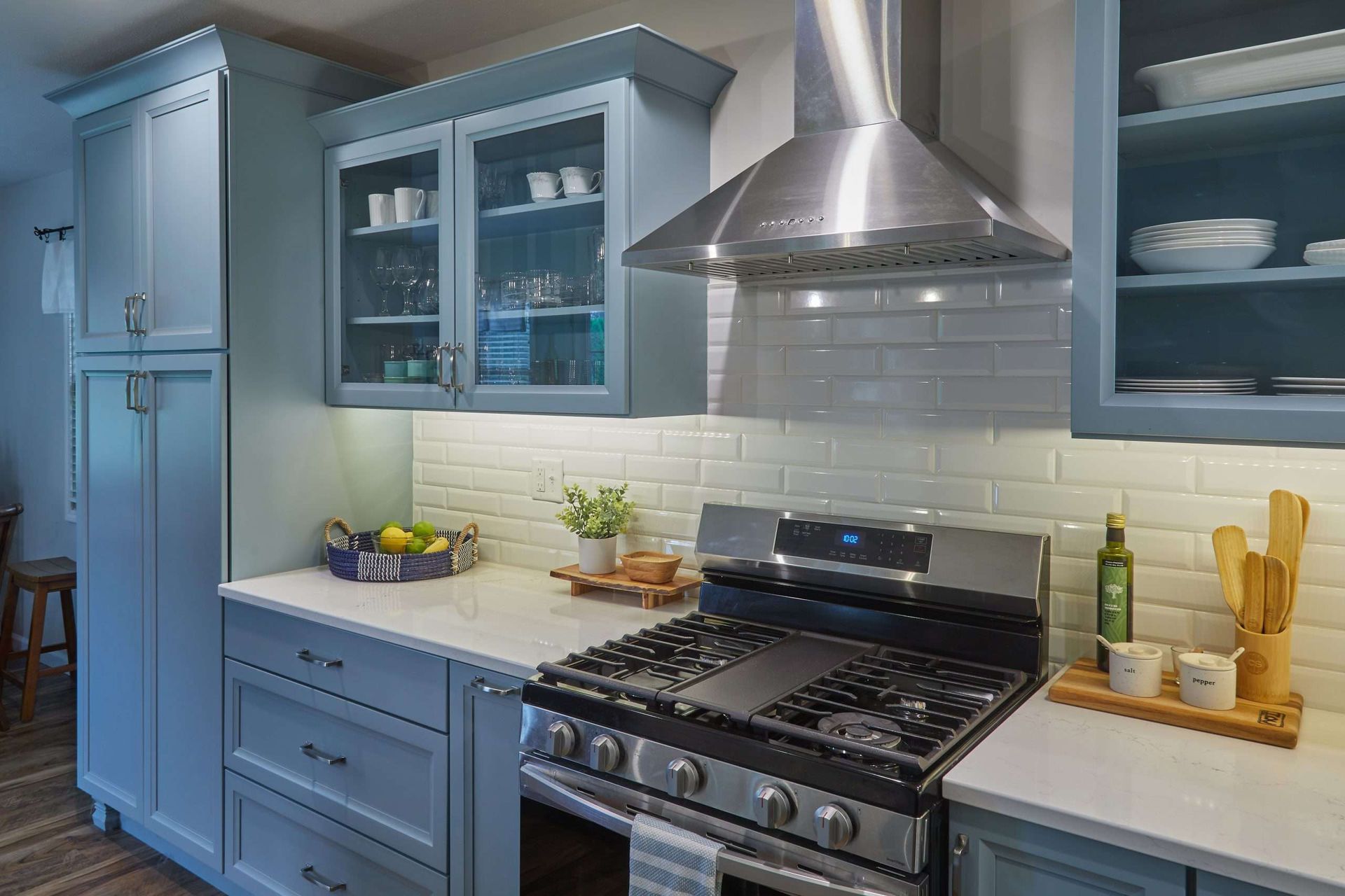 Blue kitchen with stainless steel stove, white countertops, and glass-front cabinets