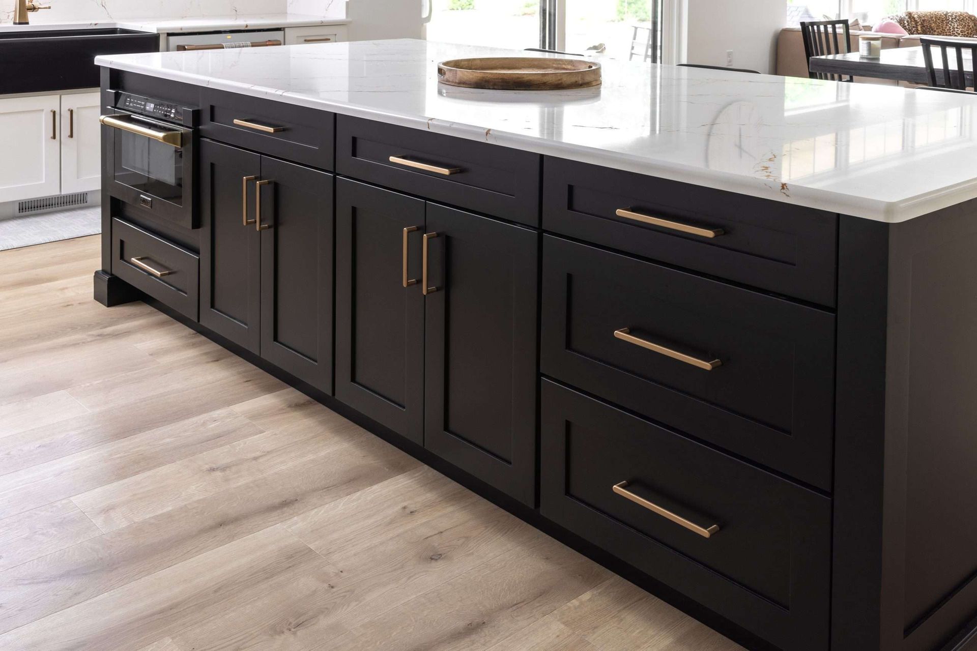 Black kitchen island with brass handles and white quartz countertop in a modern kitchen