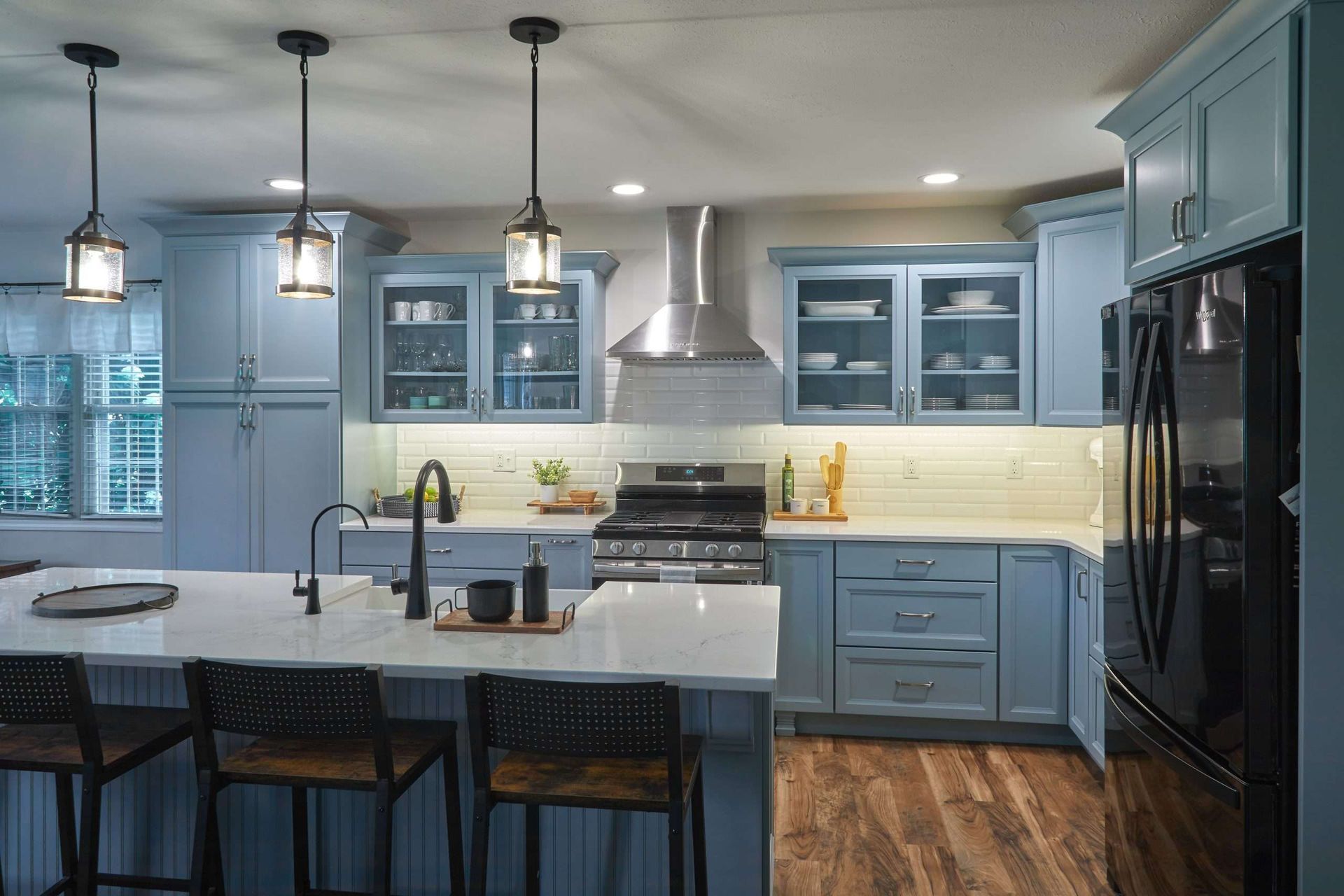 Modern kitchen with blue cabinets, white island, pendant lights, and black appliances