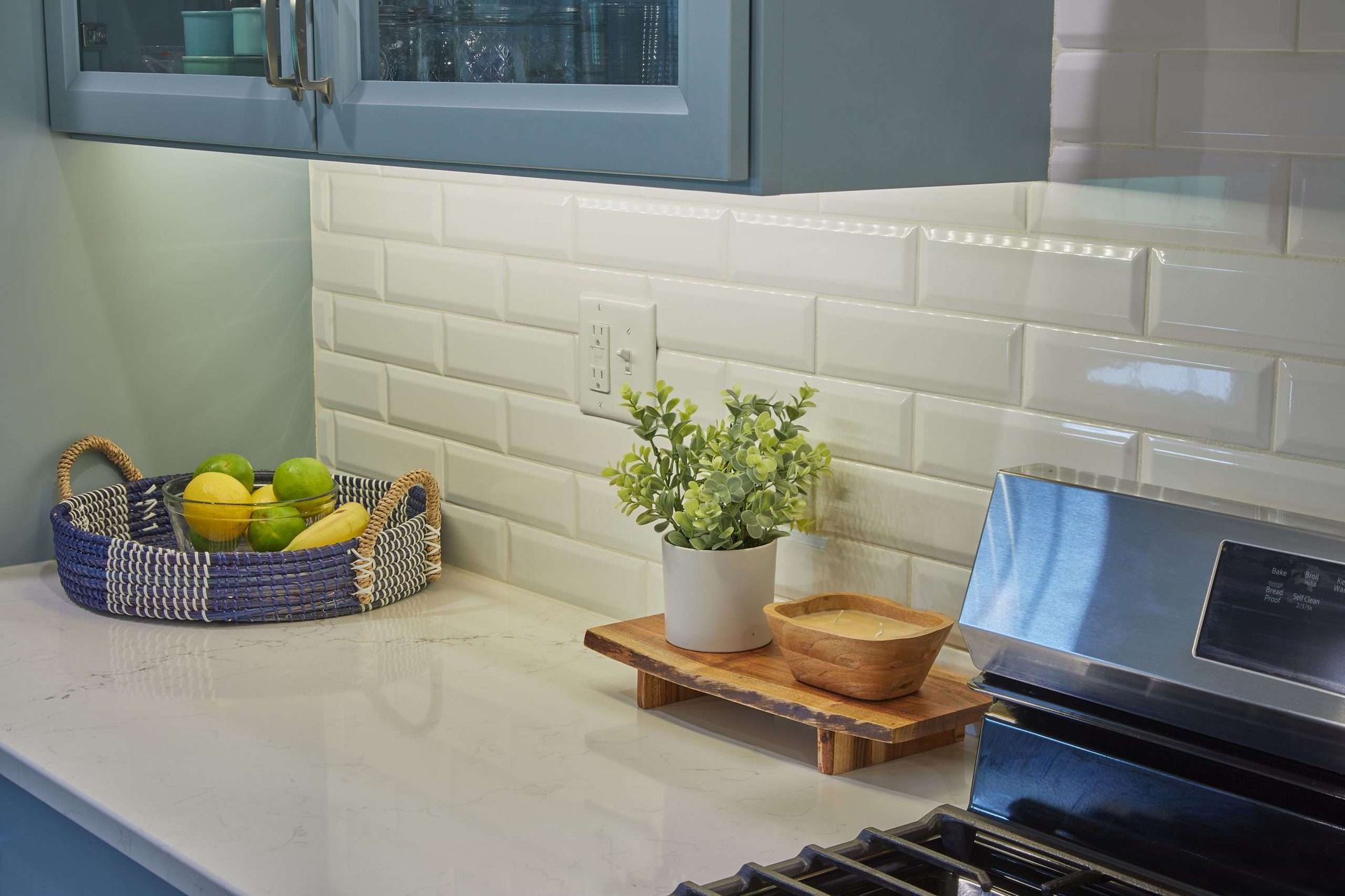 Bright kitchen counter with a fruit basket, potted herb, and wooden tray beside a stove