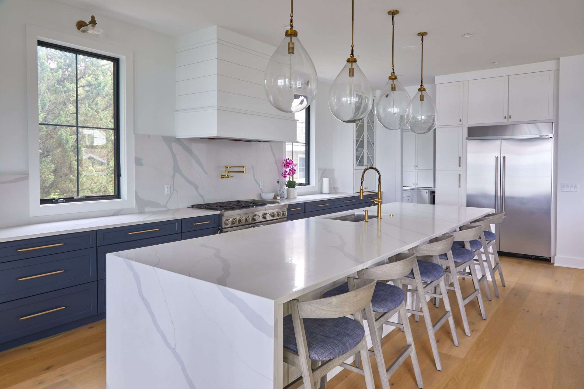 Modern white kitchen with marble island, blue lower cabinets, pendant lights, and stainless steel appliances