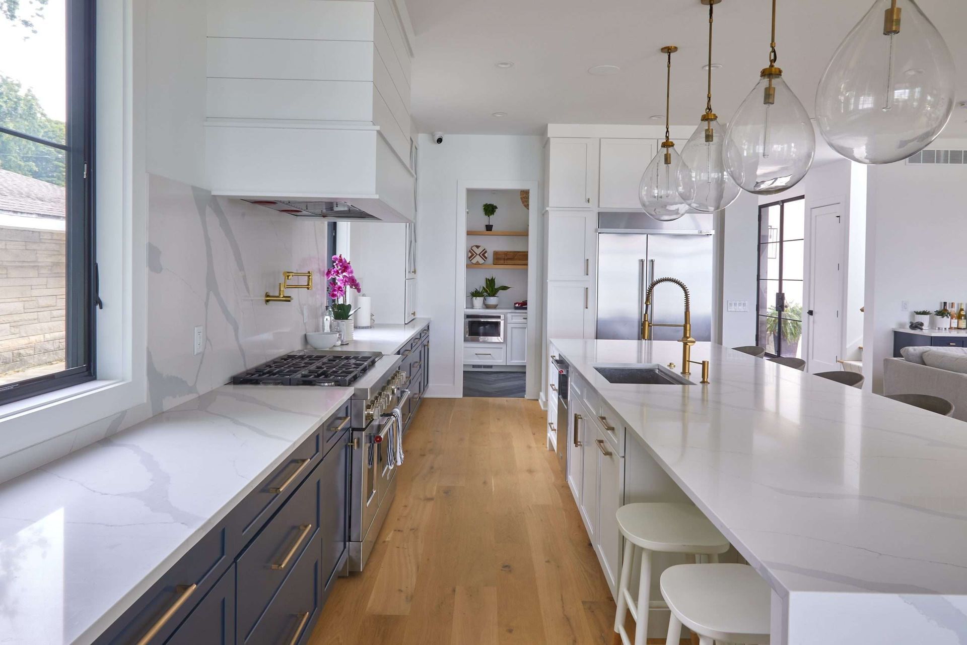 Bright modern kitchen with white island, wood floor, gray cabinets, and pendant globe lights