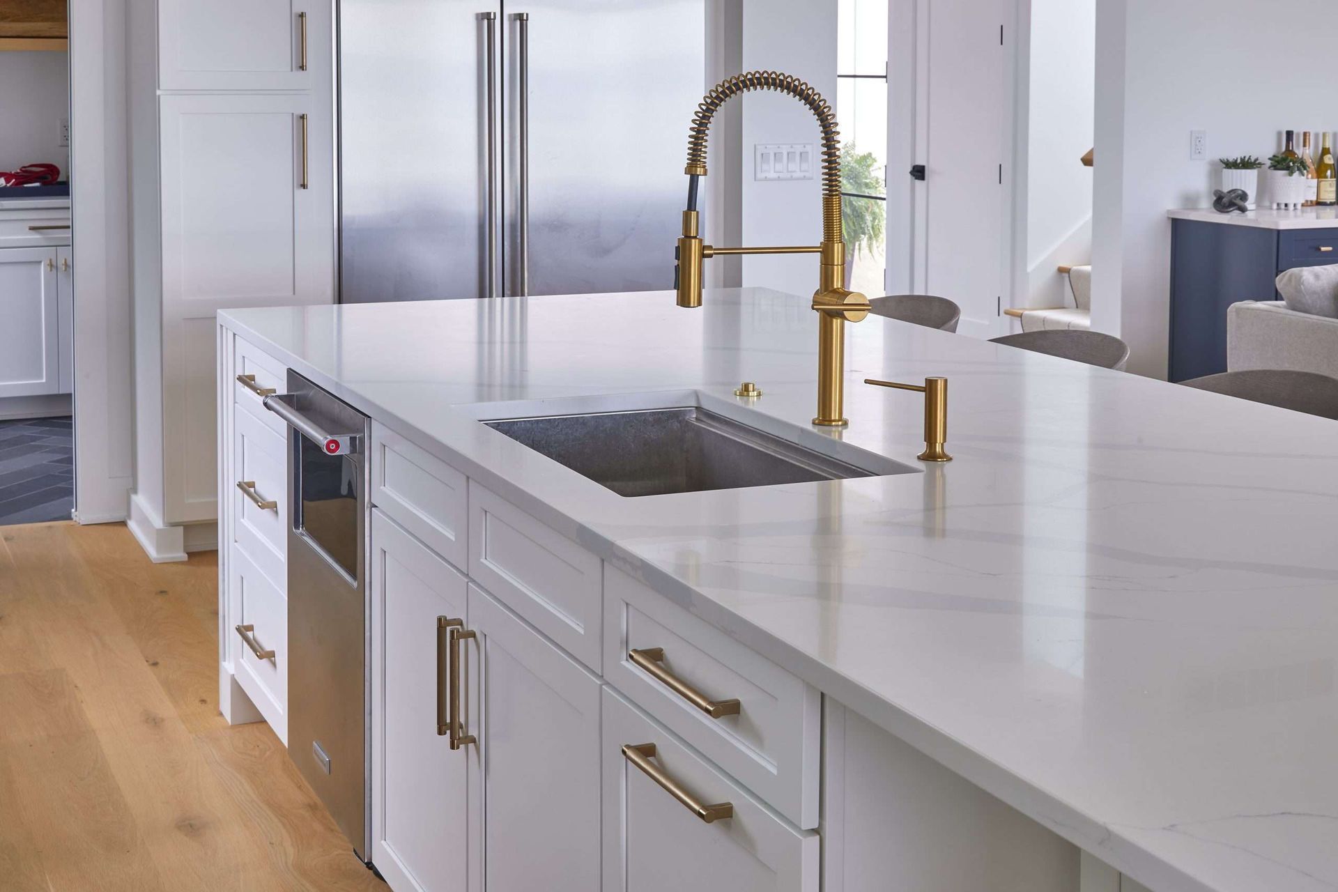 Modern white kitchen with marble island, gold faucet, and stainless steel refrigerator