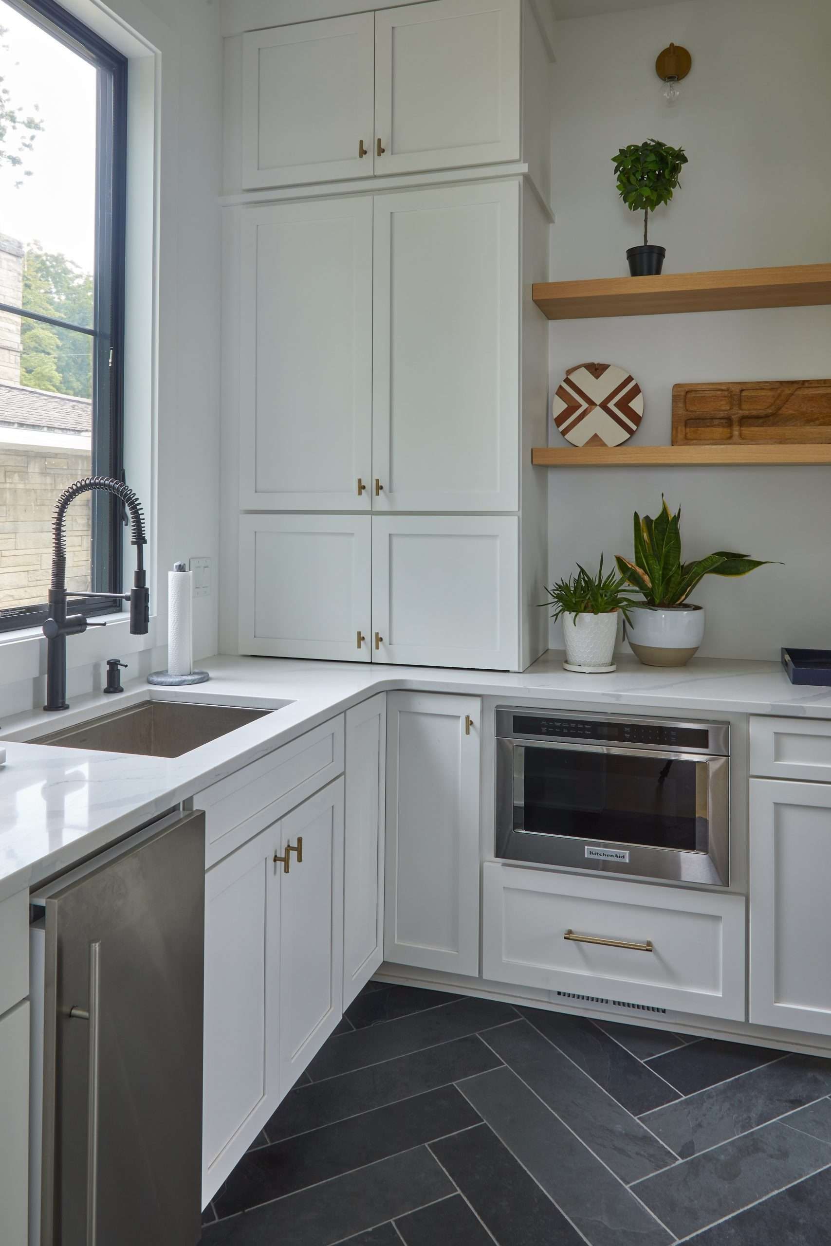 Bright white kitchen with farmhouse sink, built-in oven, open shelves, and dark herringbone floor.