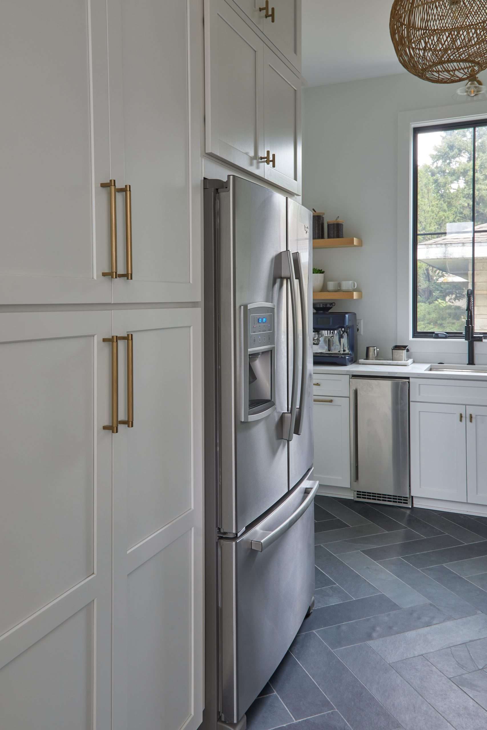 Modern white kitchen with stainless fridge, brass handles, and window by the sink