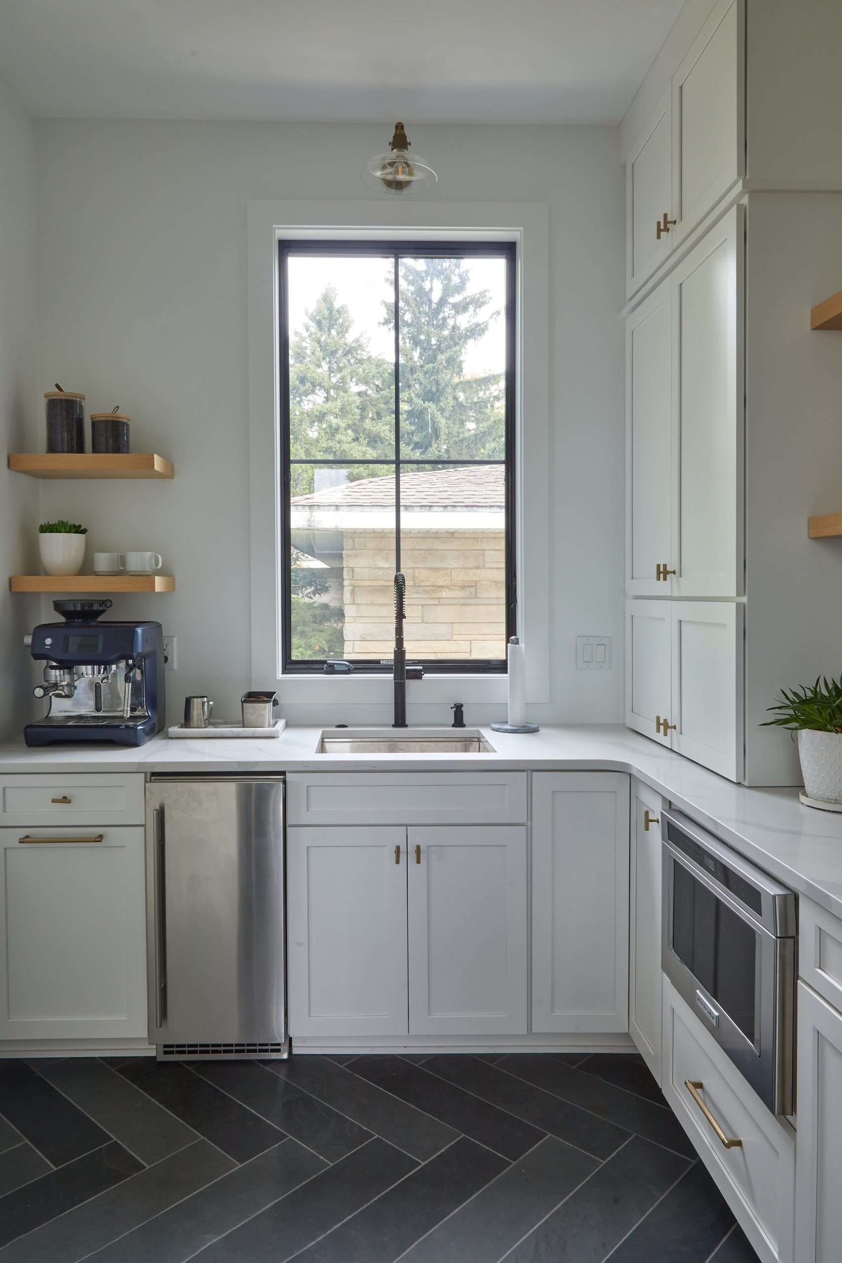 Bright white kitchen with a window above the sink, black herringbone floor, and built-in oven.