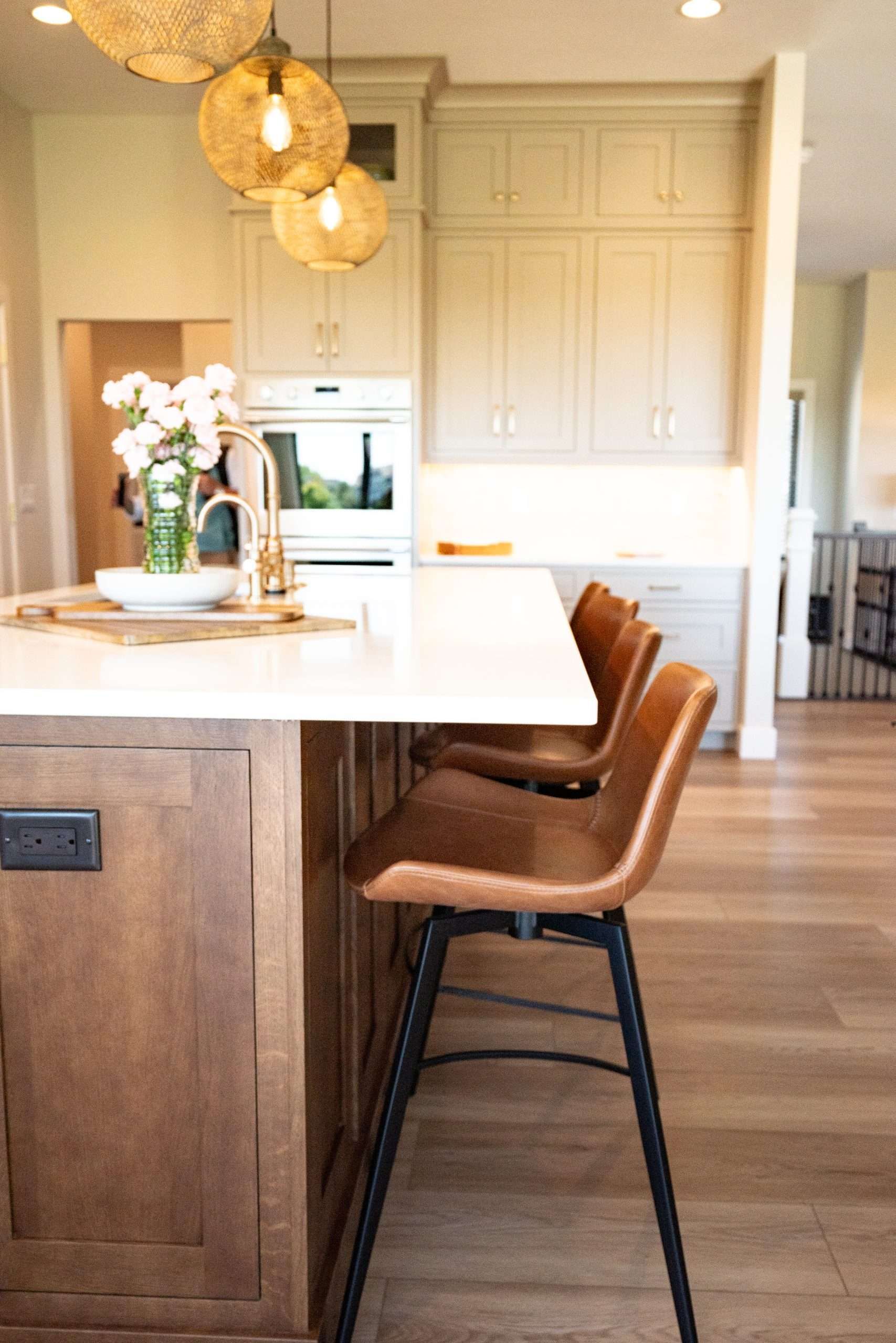 Modern kitchen with white island, tan bar stools, pendant lights, and built-in oven