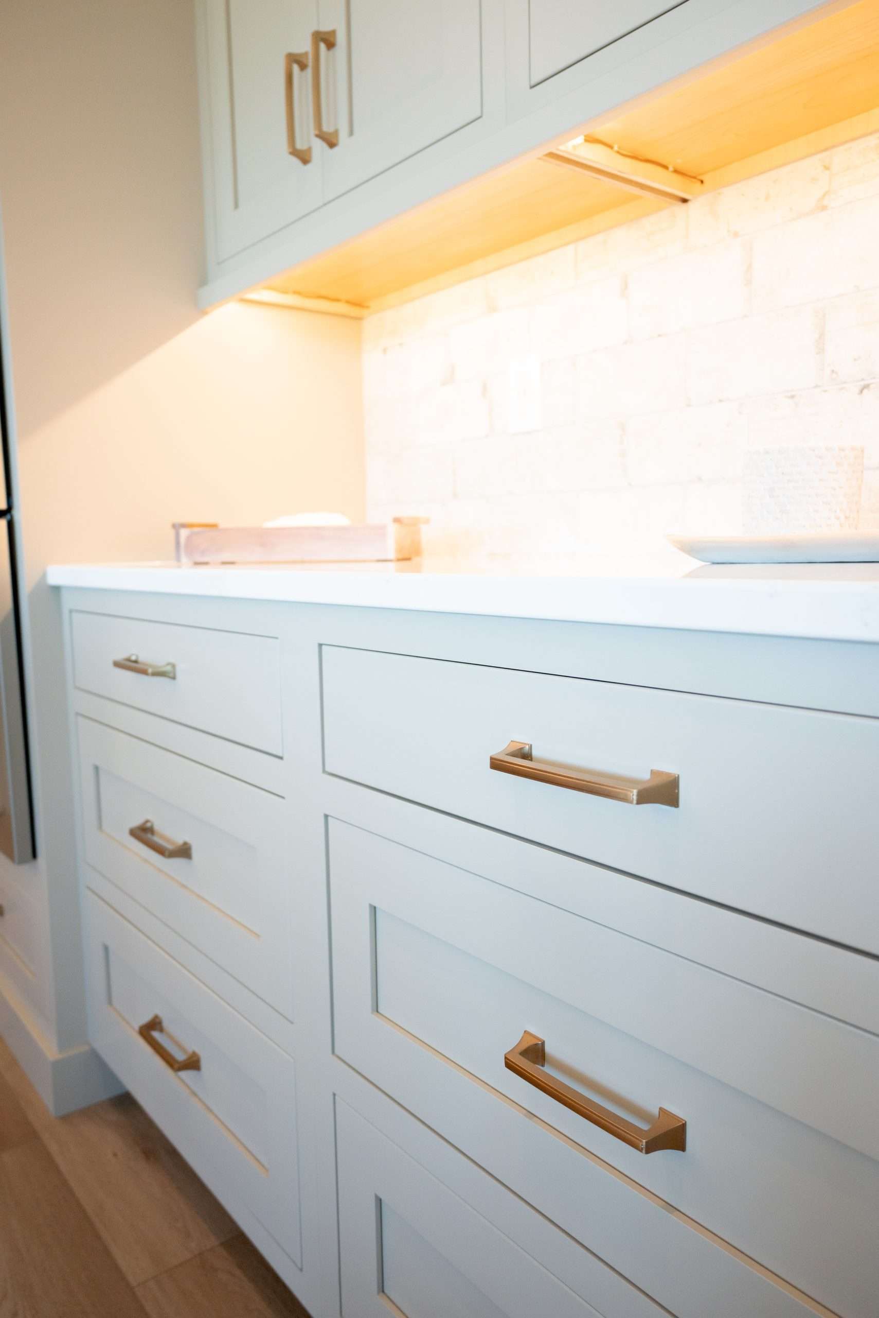 White kitchen cabinets with gold handles and under-cabinet lighting along a bright countertop