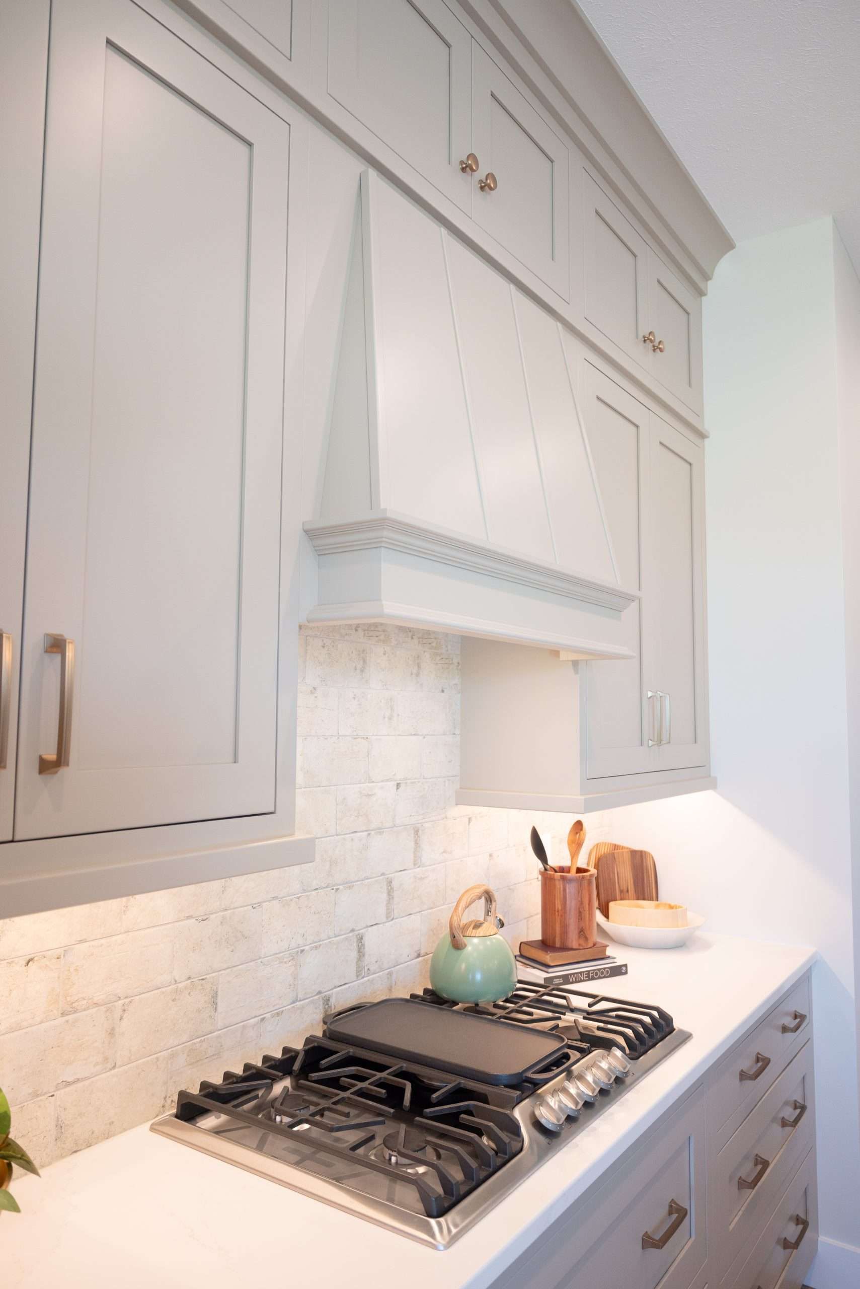 White kitchen with gas range, tiled backsplash, and beige cabinets with a range hood