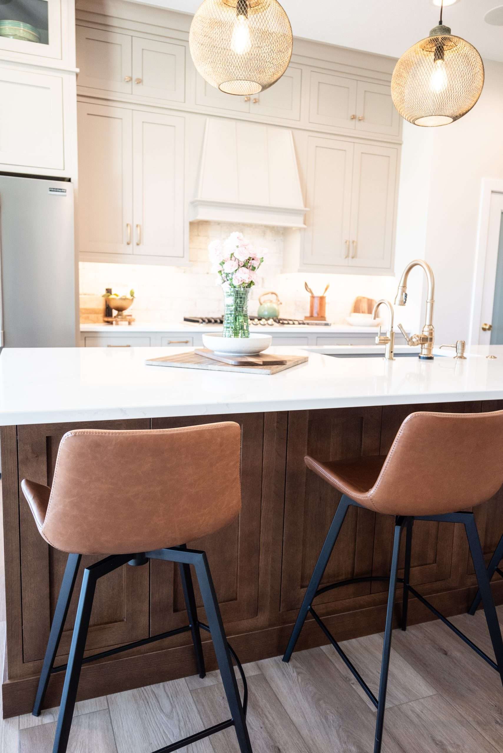 Bright modern kitchen with white cabinets, marble island, and two brown bar stools under woven pendant lights
