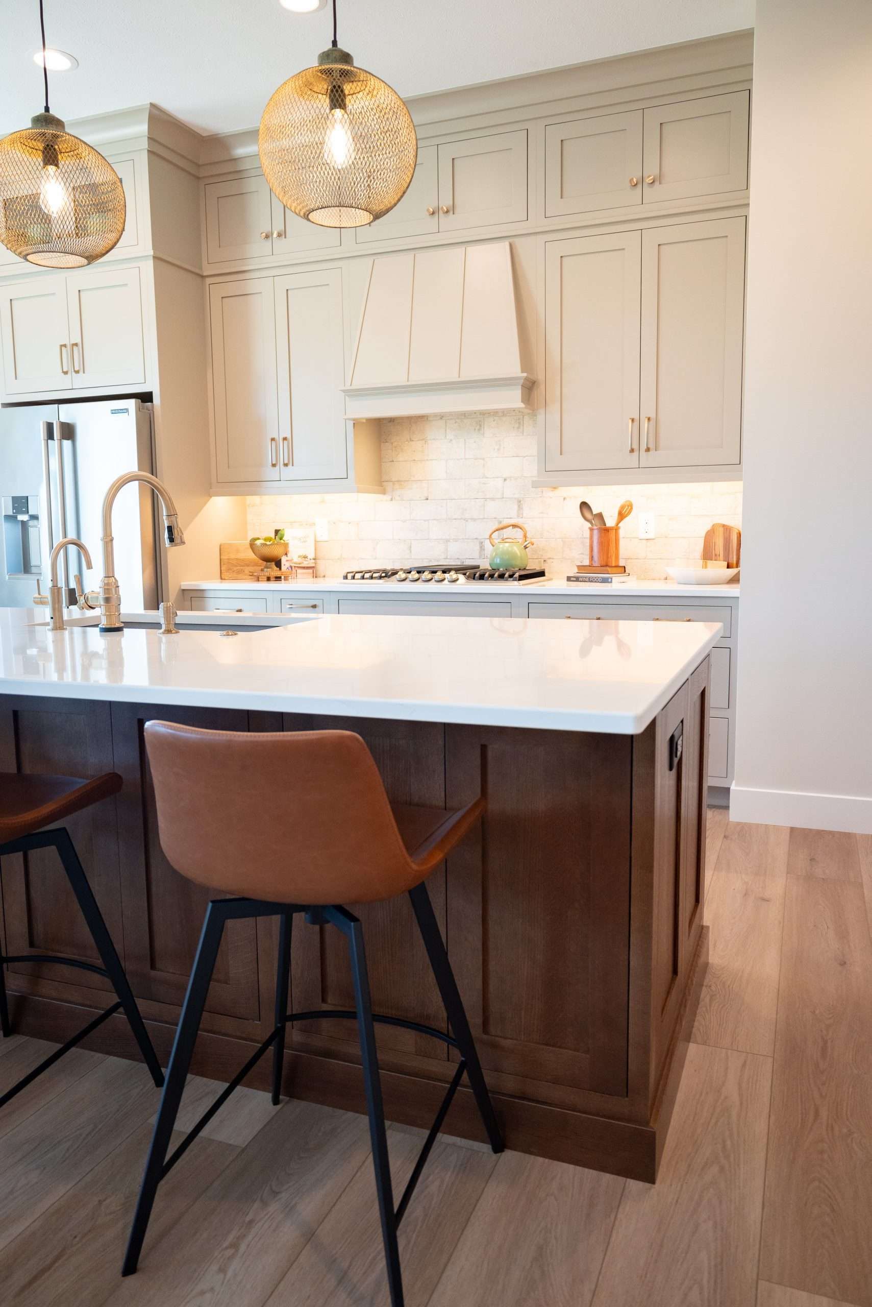Bright kitchen with a white island, brown stools, hanging pendant lights, and light wood floors