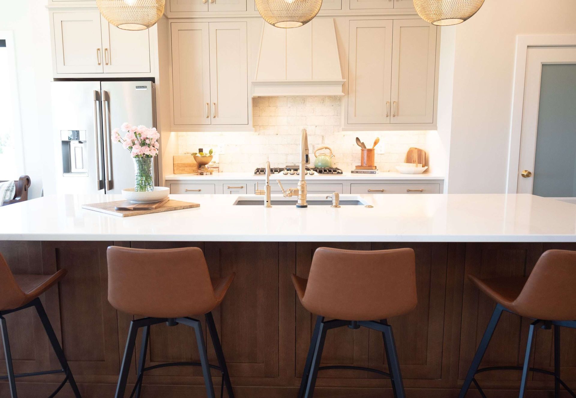 Bright modern kitchen with white cabinets, pendant lights, marble island, and four brown bar stools