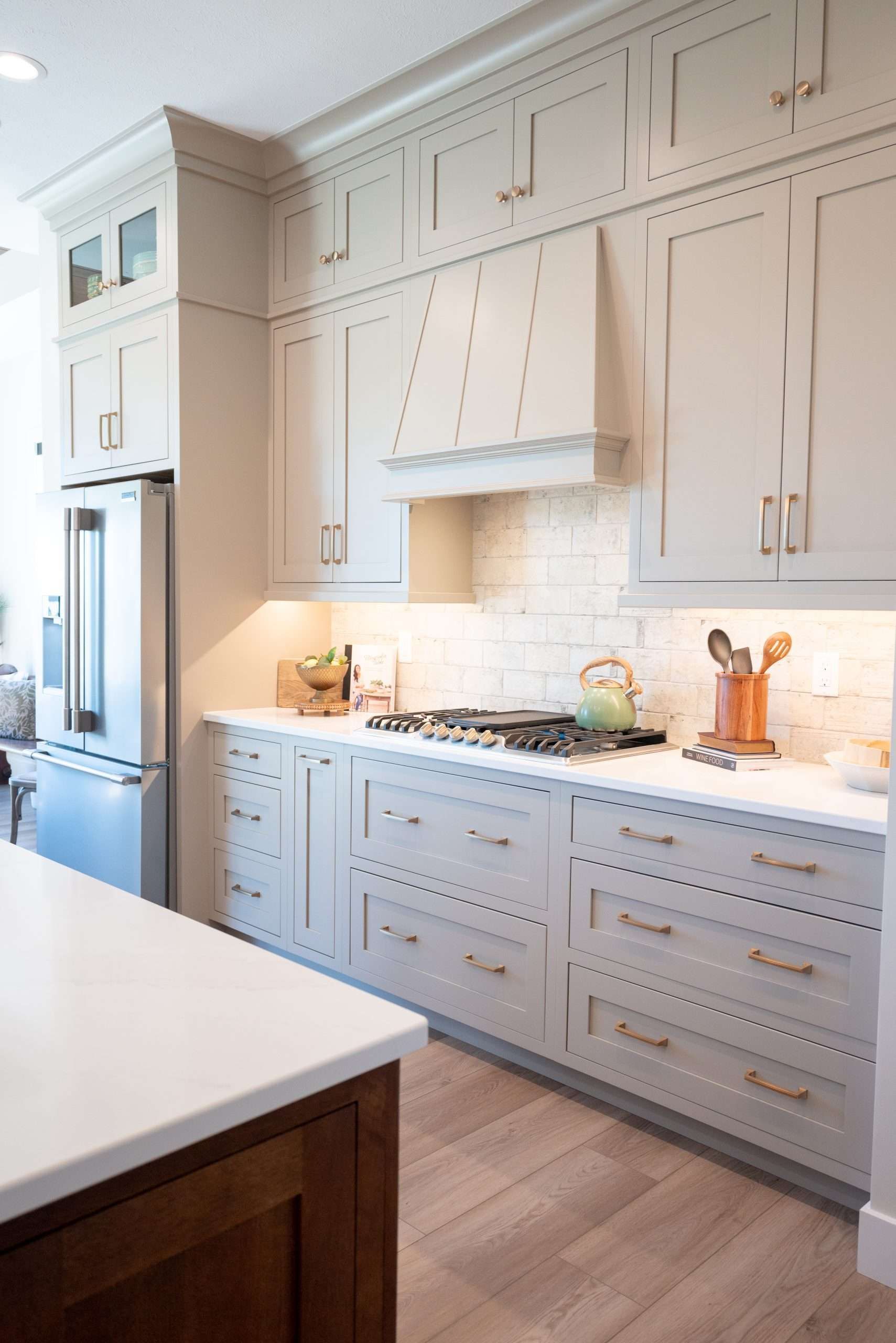 Bright white kitchen with built-in cabinets, marble backsplash, range hood, and wood floor