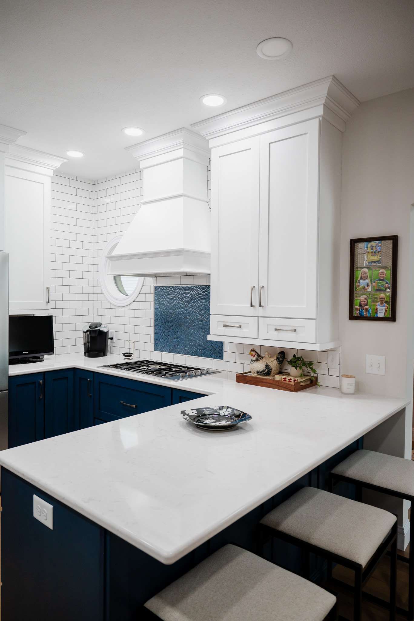 Bright white kitchen with navy cabinets, marble island, blue tile backsplash, and framed wall art