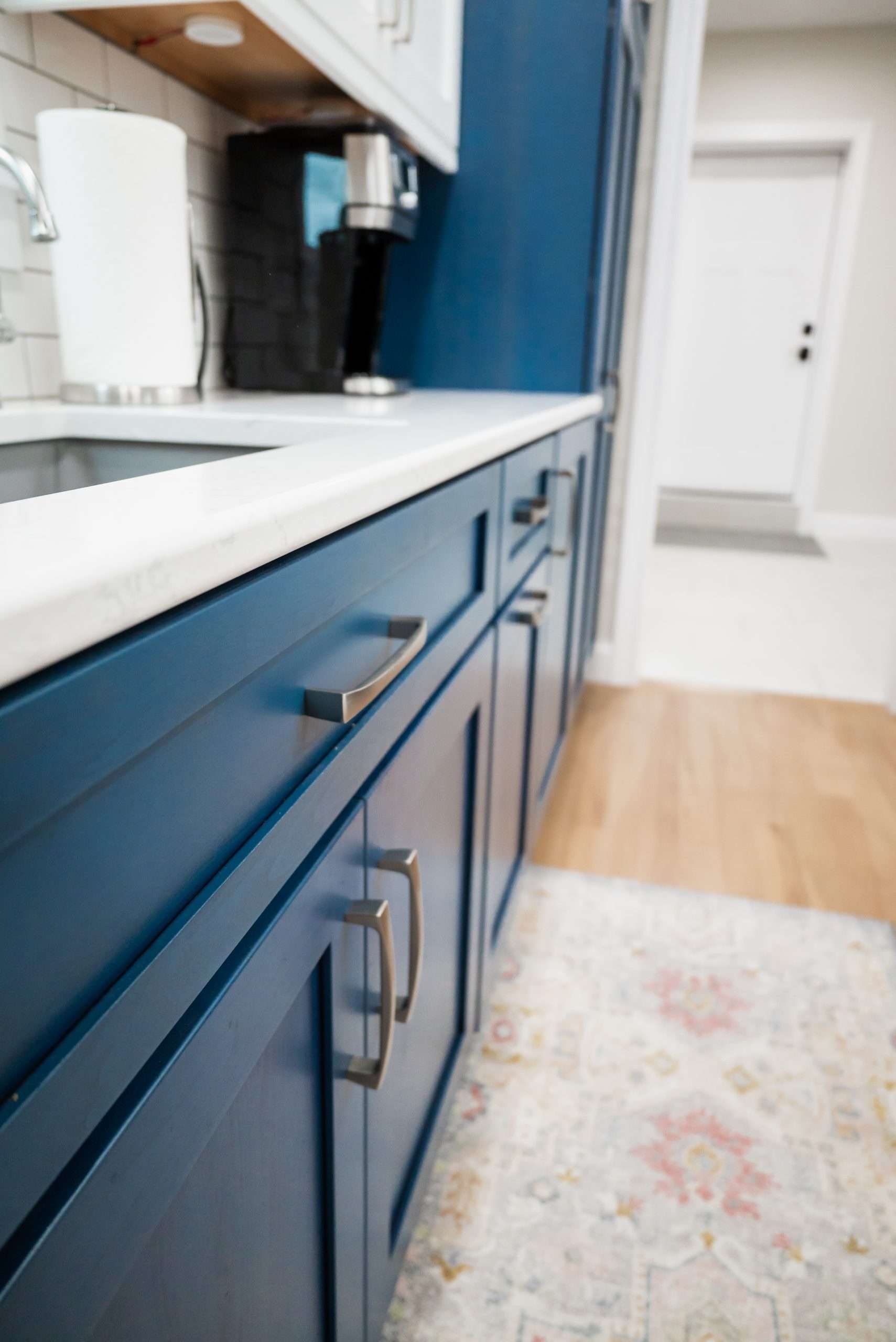Blue kitchen cabinets with a white countertop and coffee maker beside a hallway entrance.