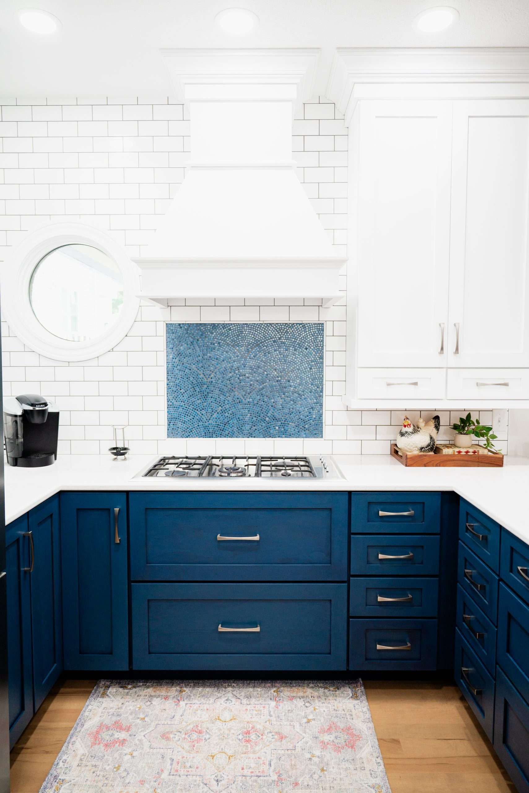 White kitchen with navy blue cabinets and a blue mosaic backsplash beneath a stovetop.