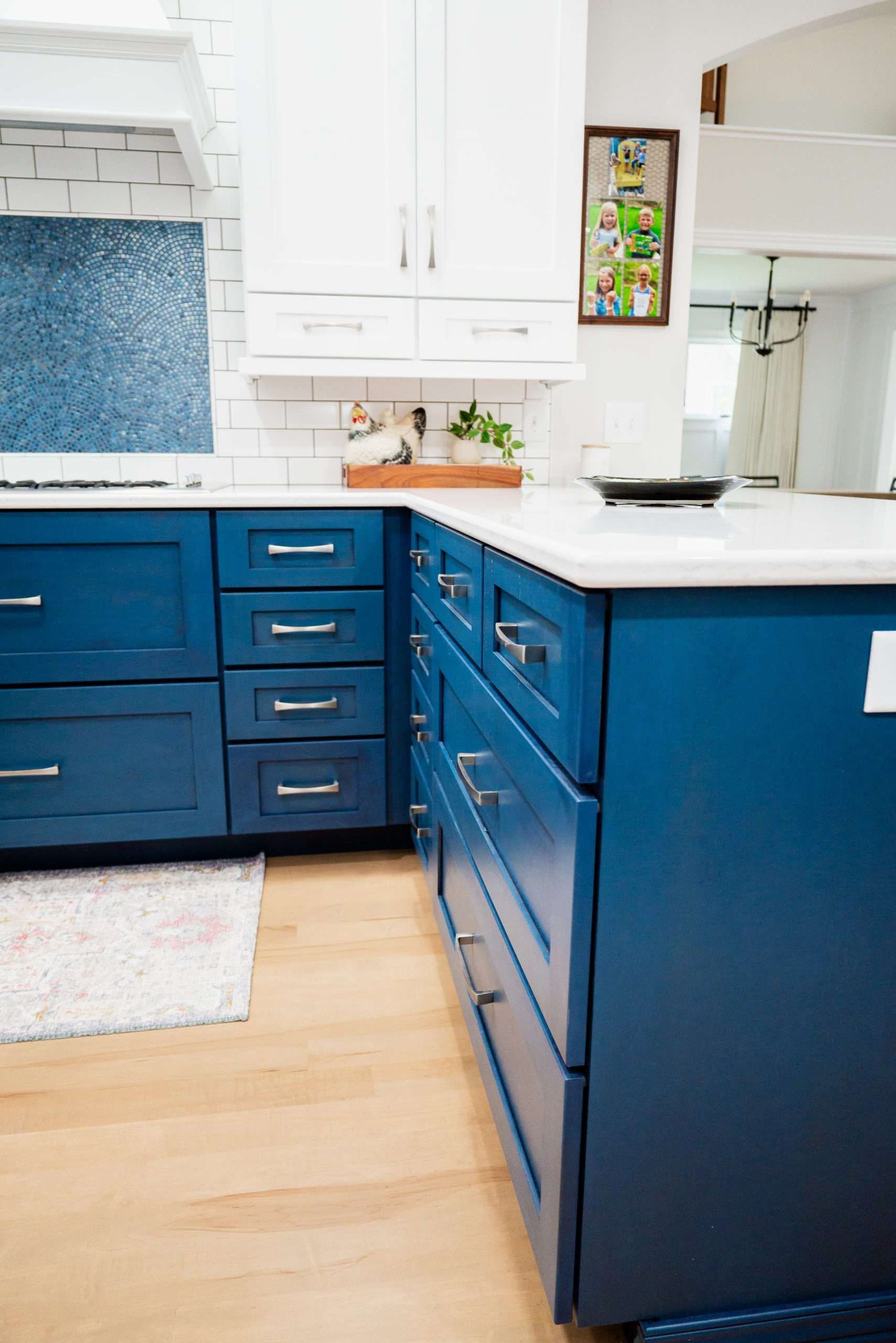 Blue kitchen cabinets with white countertops, light wood floor, and a window above the sink.