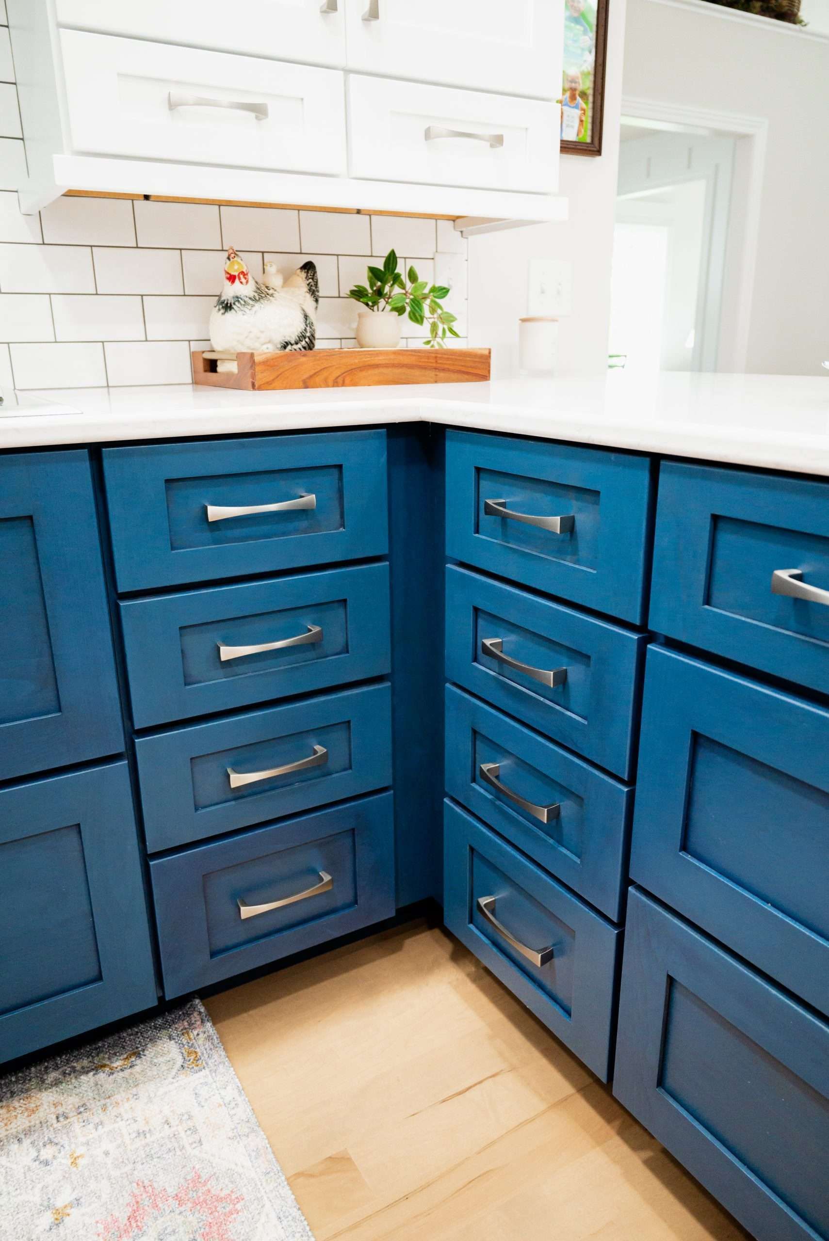 Blue kitchen cabinets with brass pulls under a white countertop and tiled backsplash.