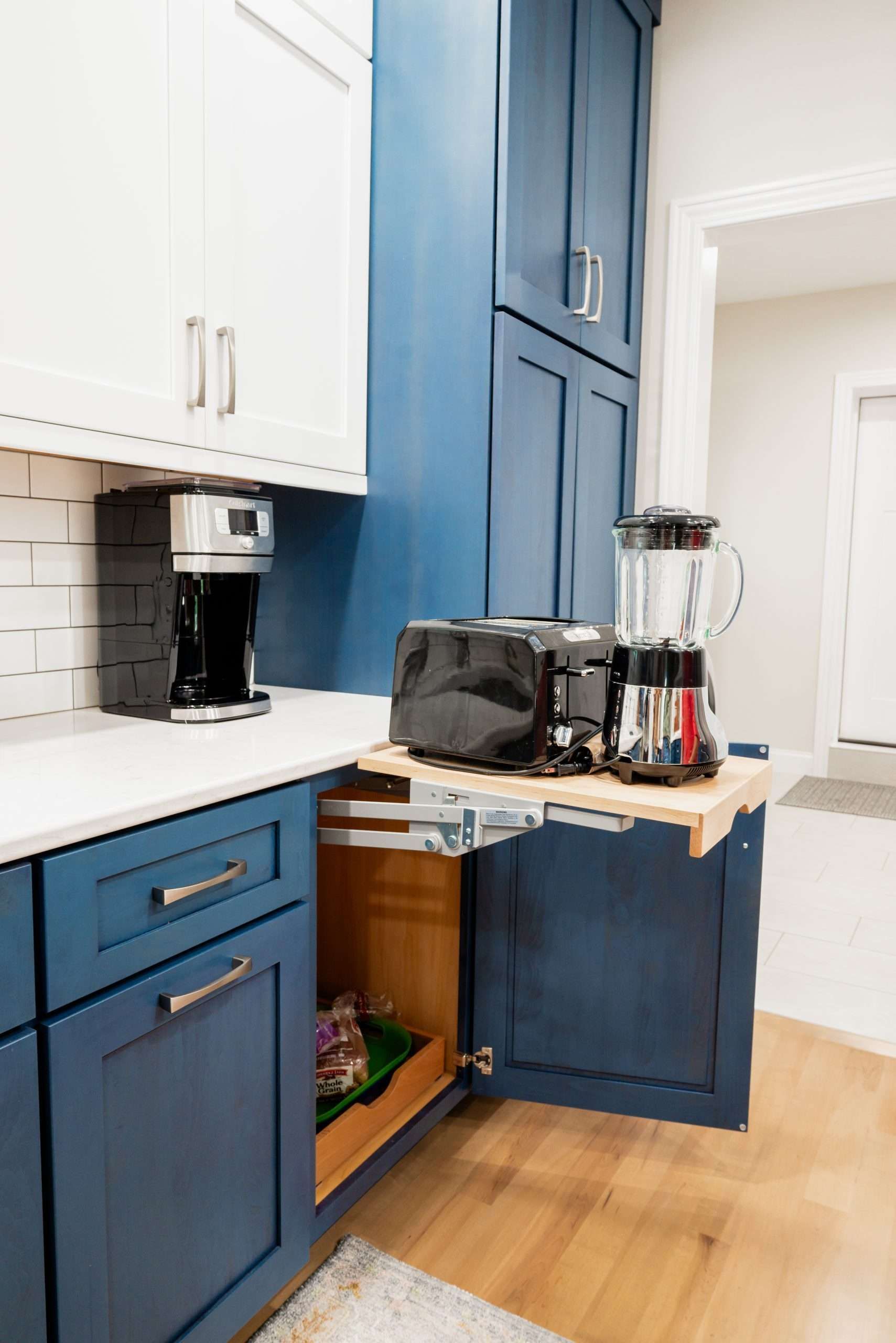 Blue kitchen corner with coffee maker, blender, toaster, and open cabinet storage under a countertop.
