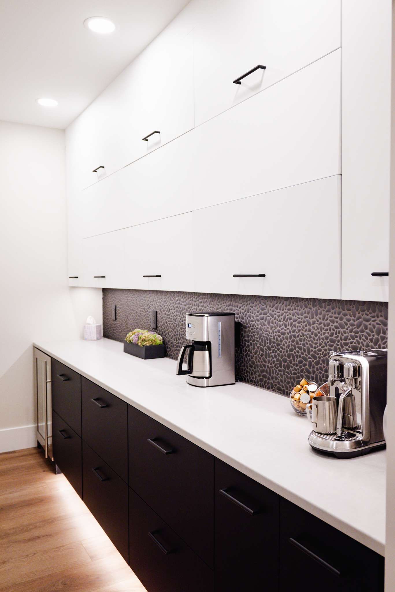 Modern white kitchen with dark lower cabinets, white countertop, and coffee maker on the counter.