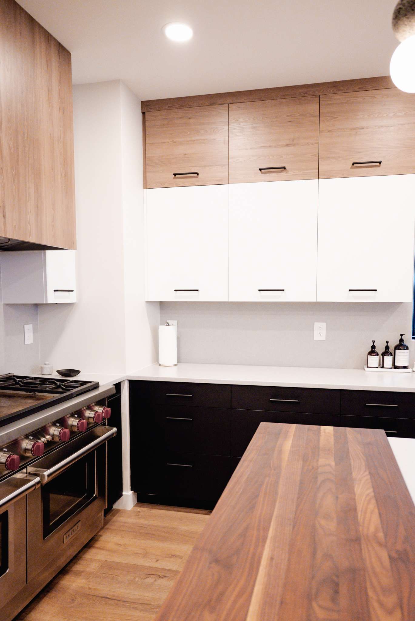 Modern kitchen with wood island, white cabinets, black lower cabinets, and stainless steel oven.