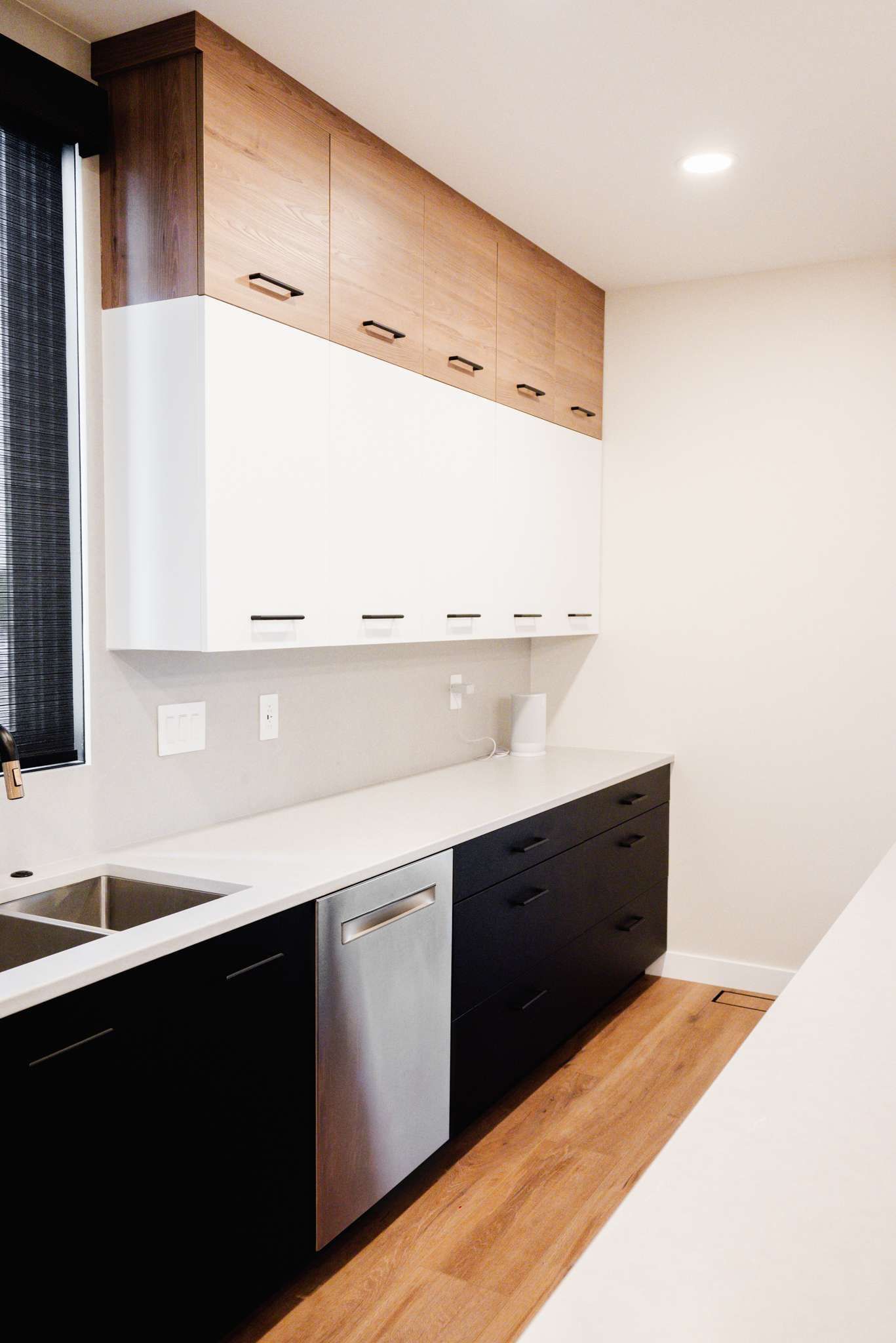 Modern kitchen with white upper cabinets, dark lower cabinets, stainless dishwasher, and wood floor.