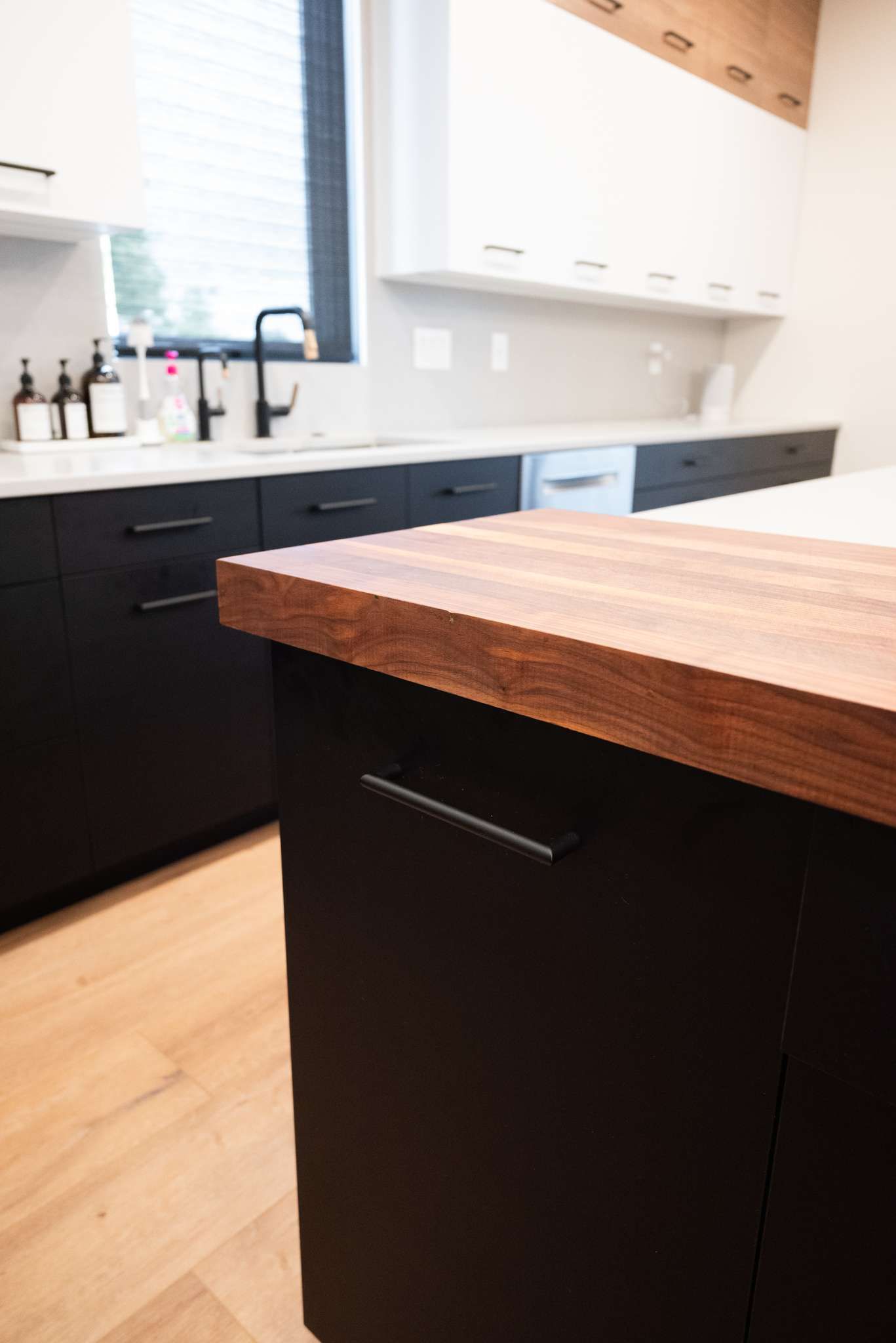 Modern kitchen with black and white cabinets, light wood floor, and a butcher block island countertop