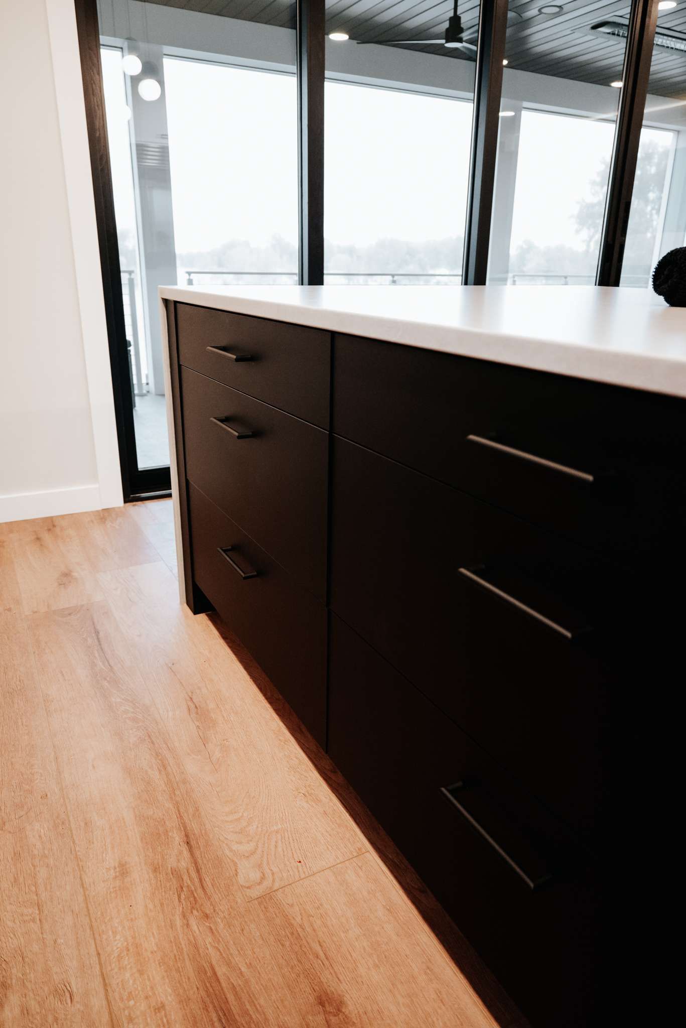 Modern kitchen island with dark cabinets and white countertop in a bright room with large windows