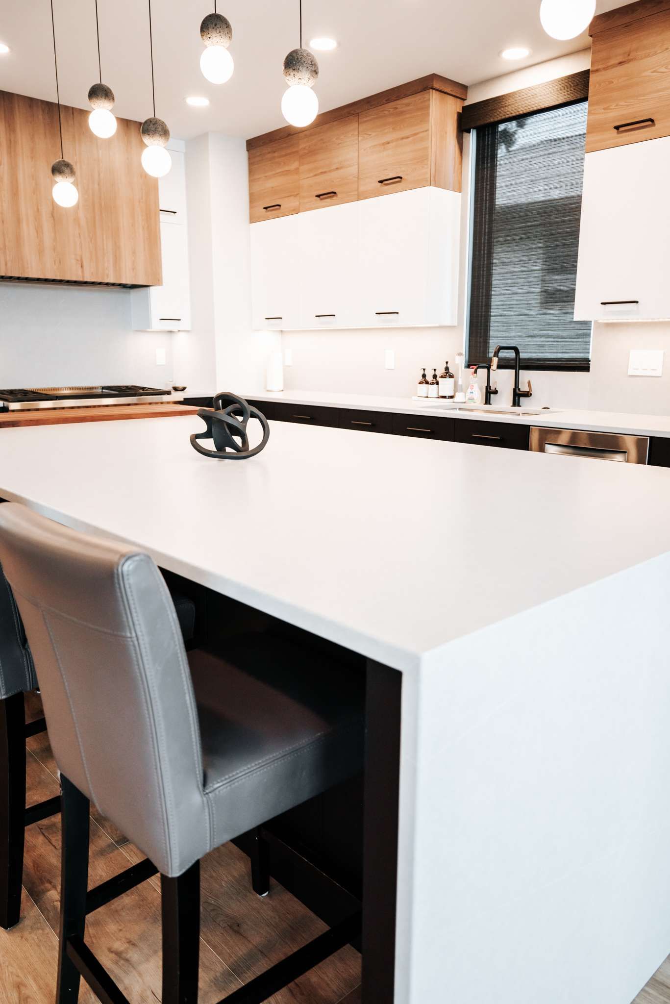 Modern kitchen with white island, pendant lights, wood cabinets, and gray chair near a window