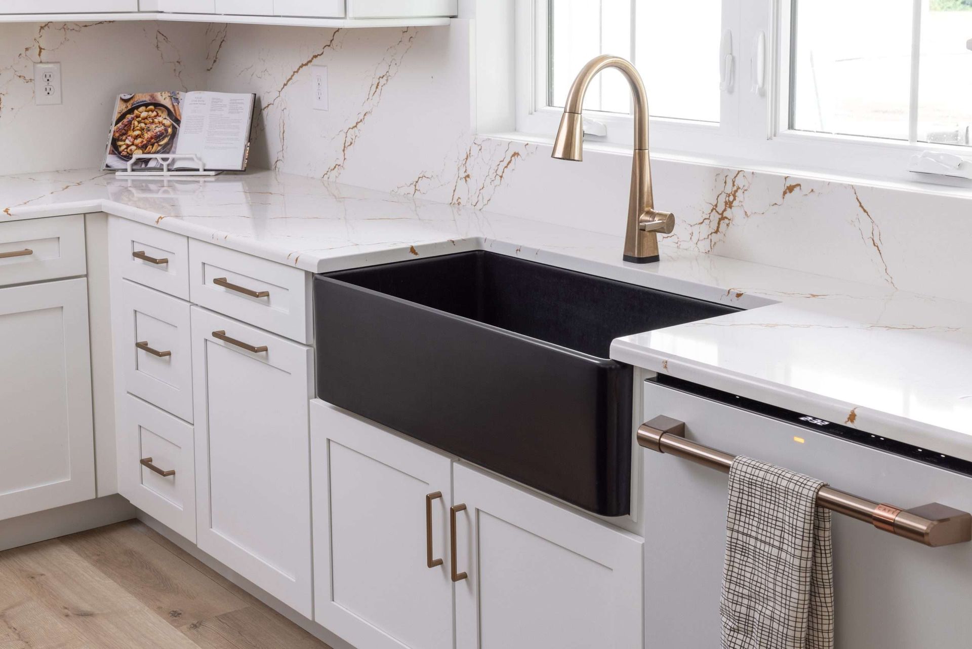 Modern kitchen sink with black apron front, white cabinets, gold faucet, and marble countertop
