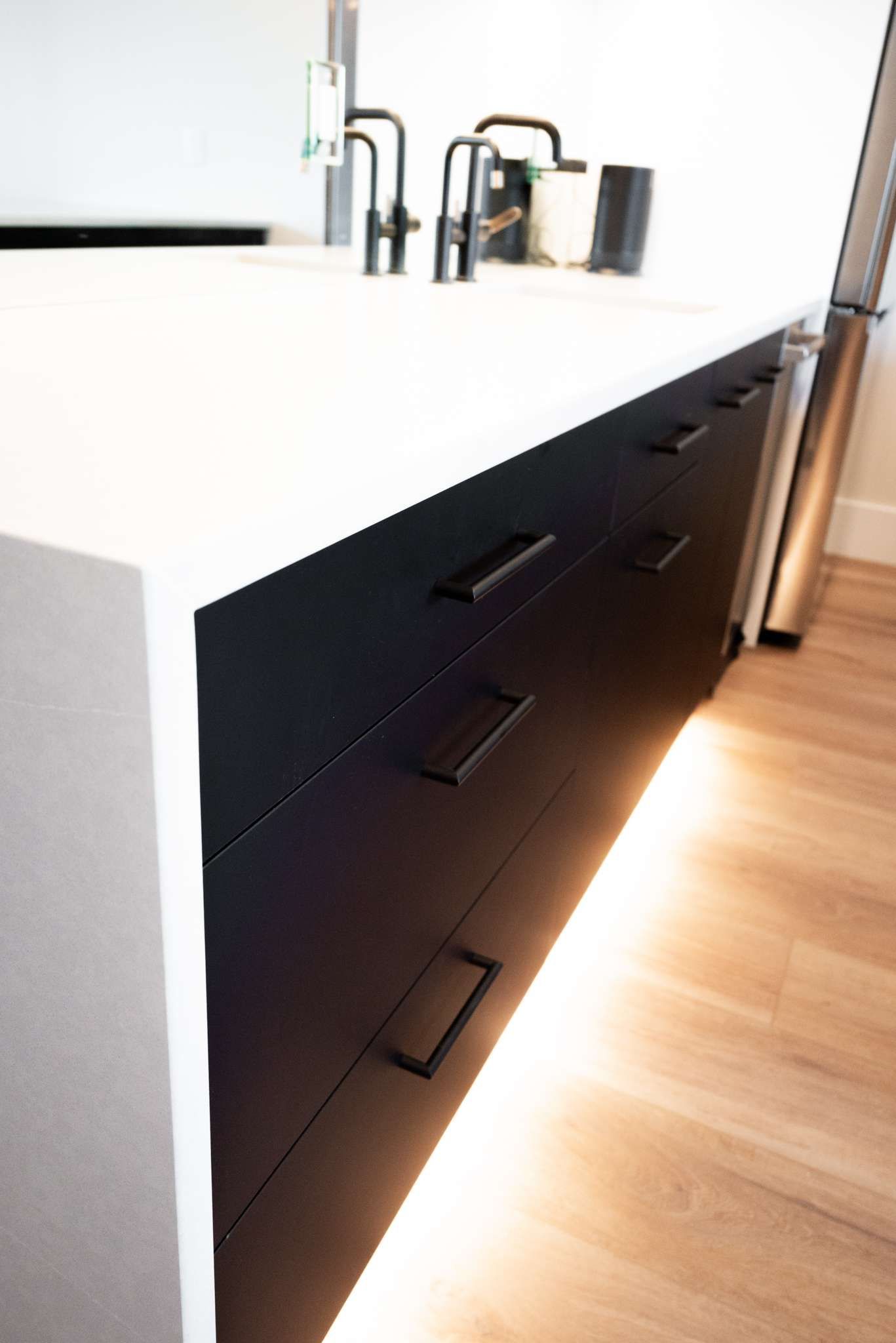 Modern kitchen island with white countertop, black drawers, and chrome faucet on wood floor
