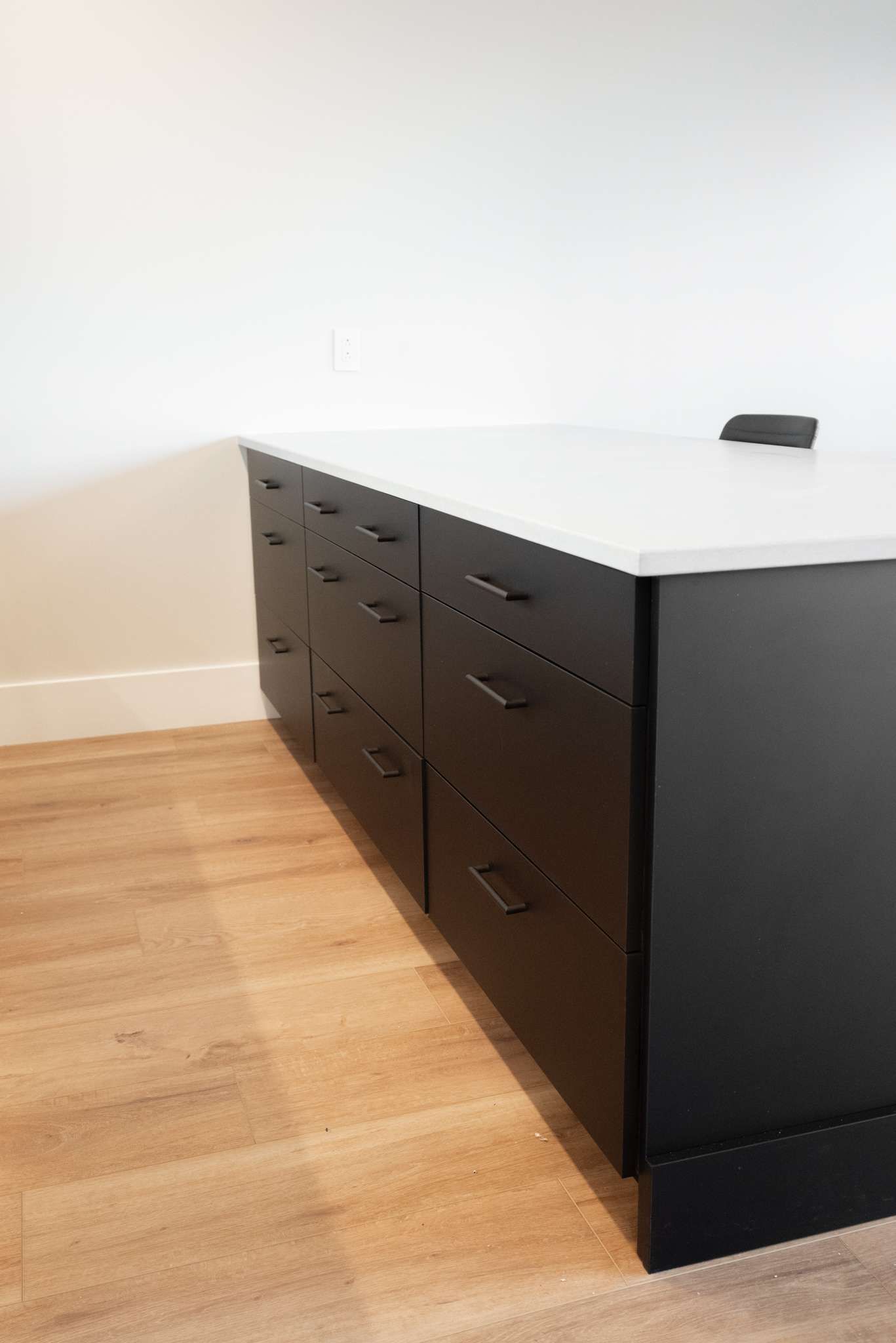 Black office desk with drawers on a light wood floor against a white wall.