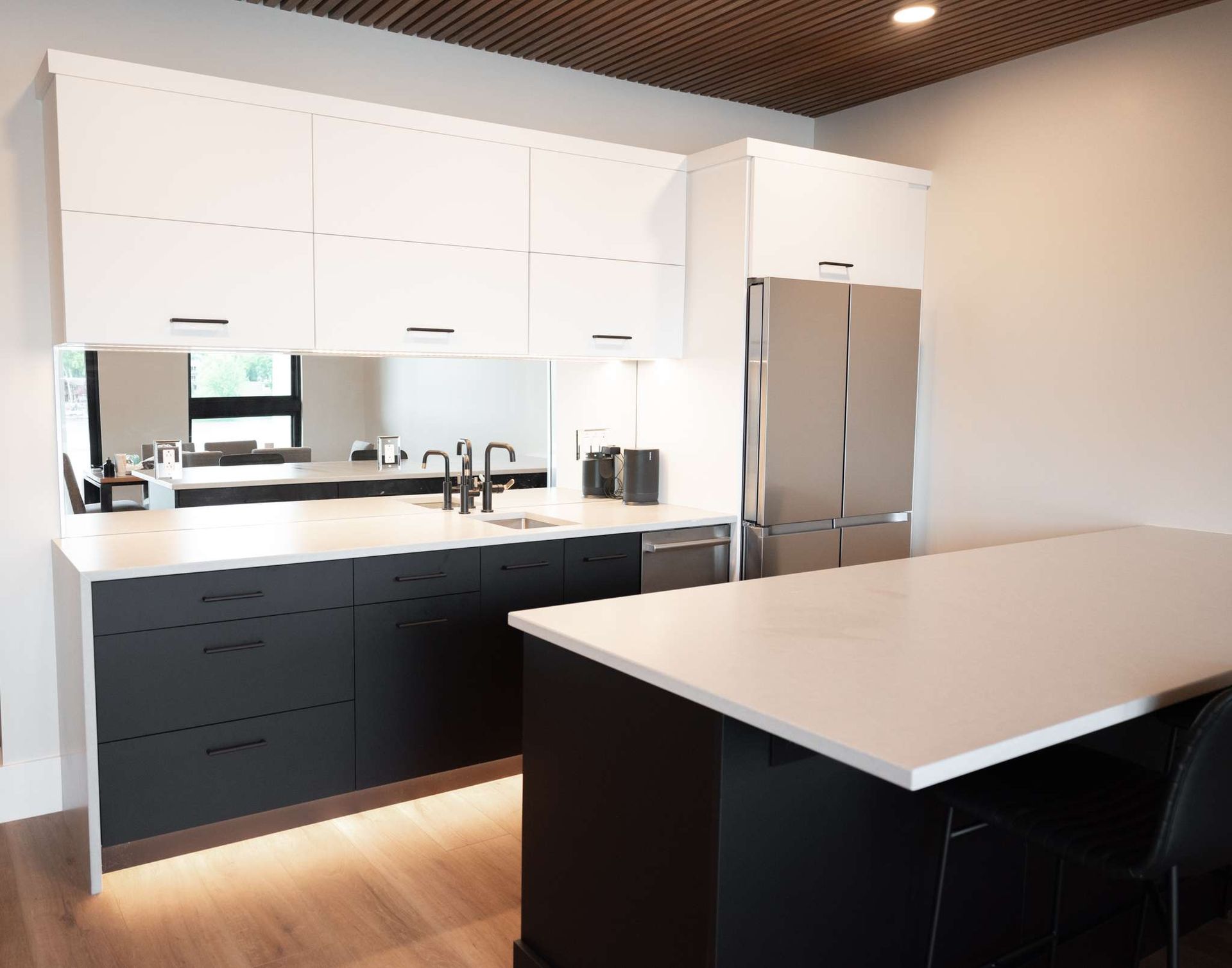 Modern kitchen with white cabinets, black lower cabinets, stainless fridge, and a large island with white countertop
