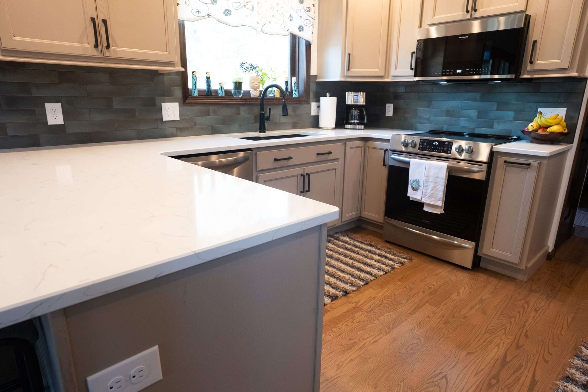 Modern kitchen with white countertops, gray cabinets, stainless appliances, and wood flooring