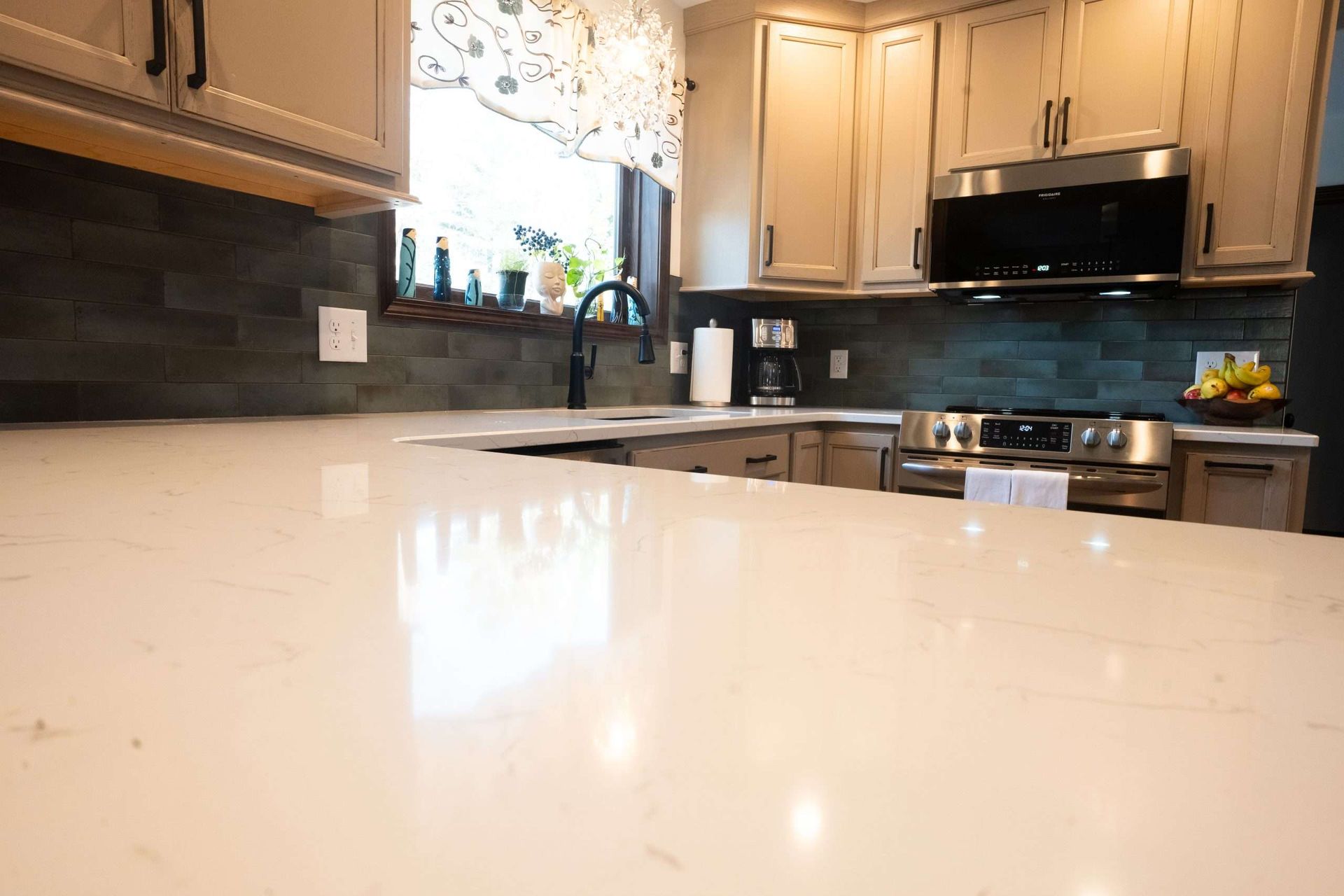 Modern kitchen with light wood cabinets, black appliances, and a glossy white countertop