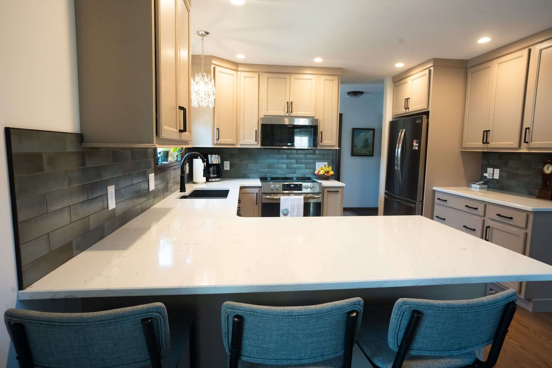 Modern kitchen with white island, dark tile backsplash, stainless appliances, and blue bar stools