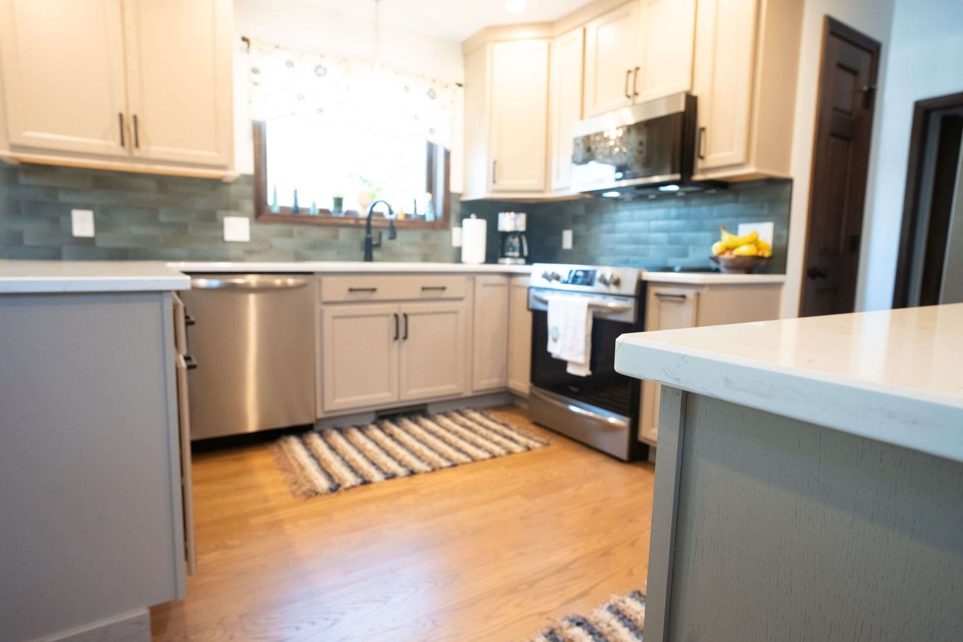Bright kitchen with white cabinets, stainless appliances, and a striped rug on a wooden floor.