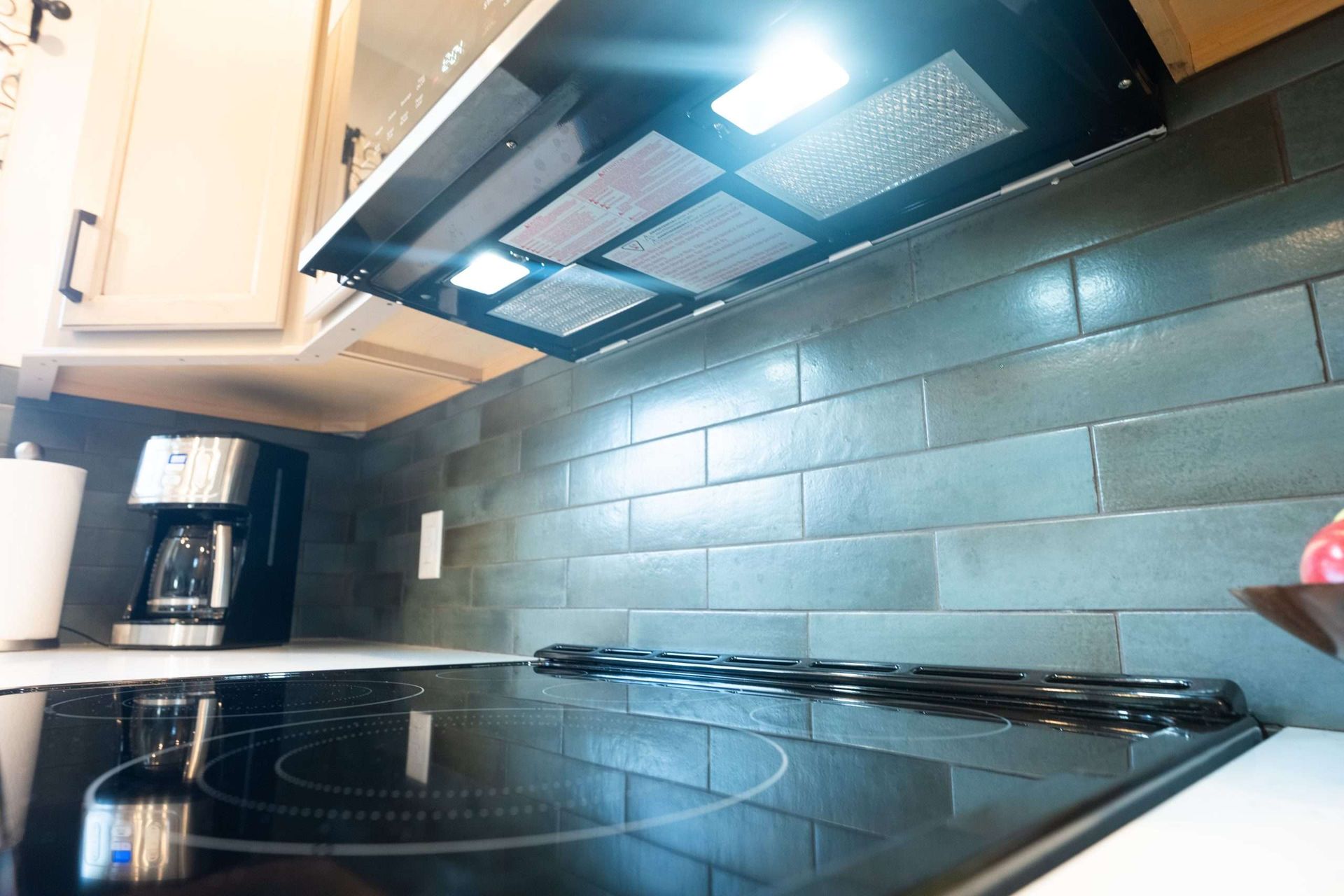 Modern kitchen with black glass stove, blue tile backsplash, and range hood under cabinet lighting
