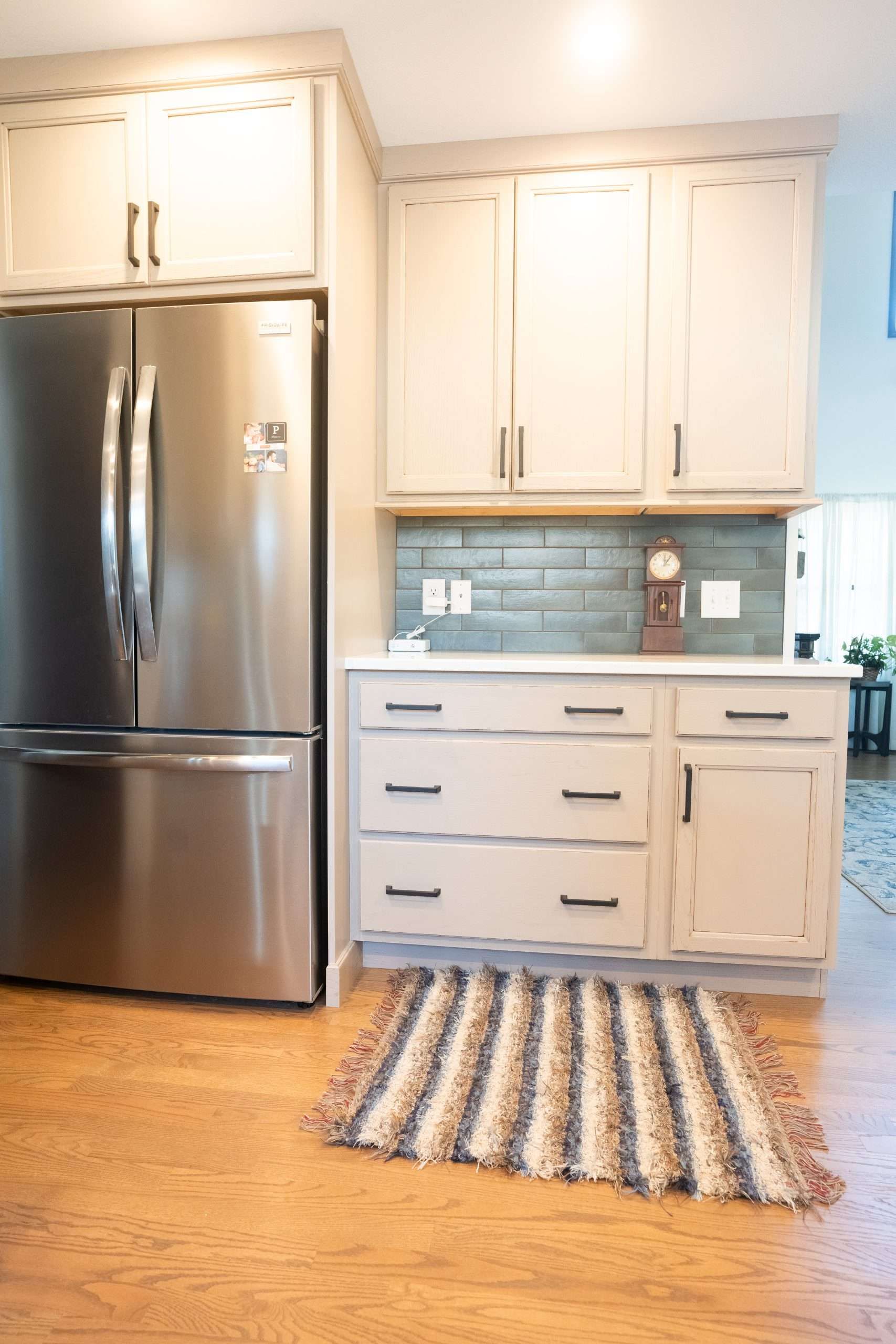 Bright kitchen with stainless steel fridge, white cabinets, blue tile backsplash, and a striped rug.